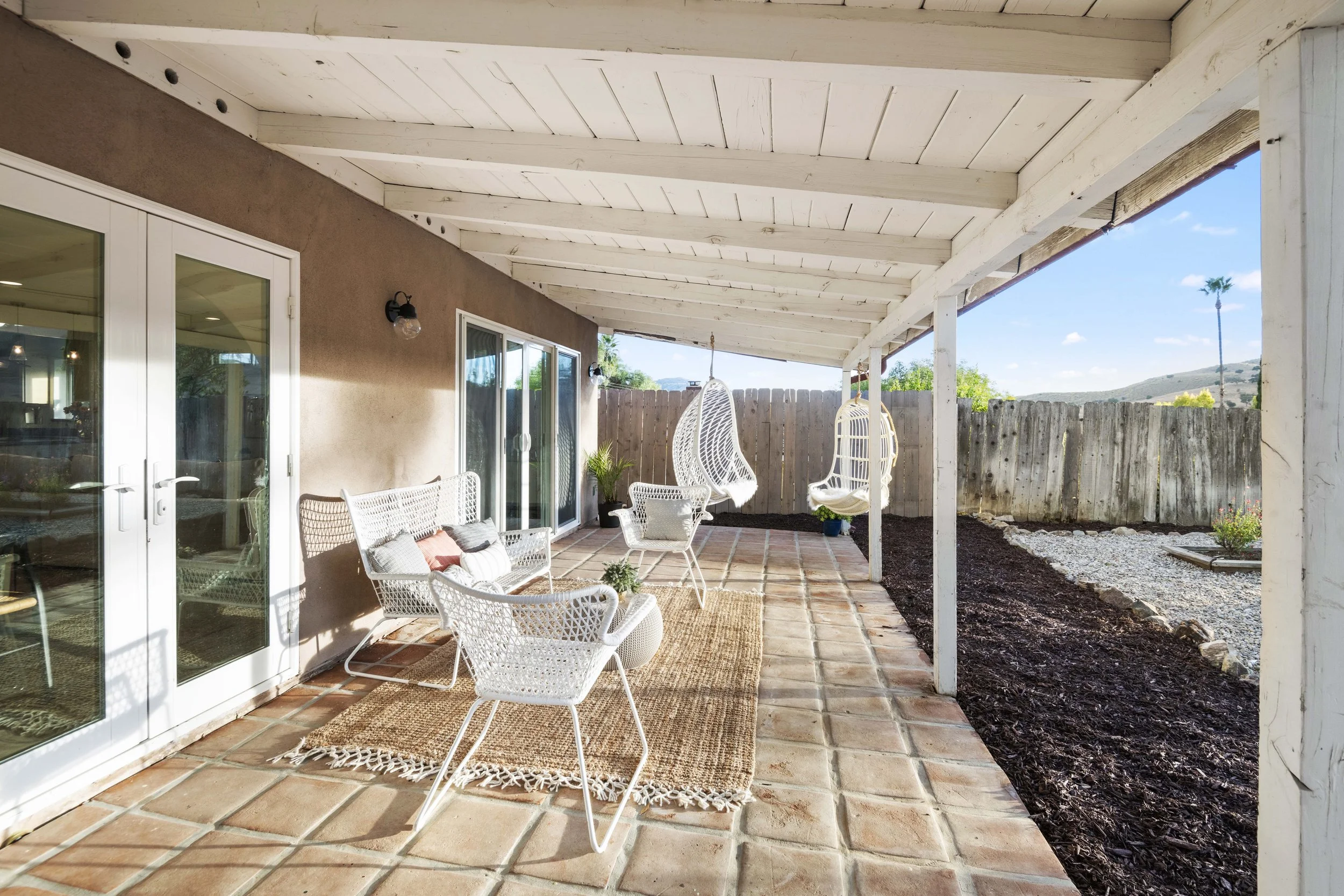 Affordable LA backyard patio with rustic tile, hanging wicker chairs, and mountain backdrop — captured by Intuition Real Estate Media for elegant outdoor staging.