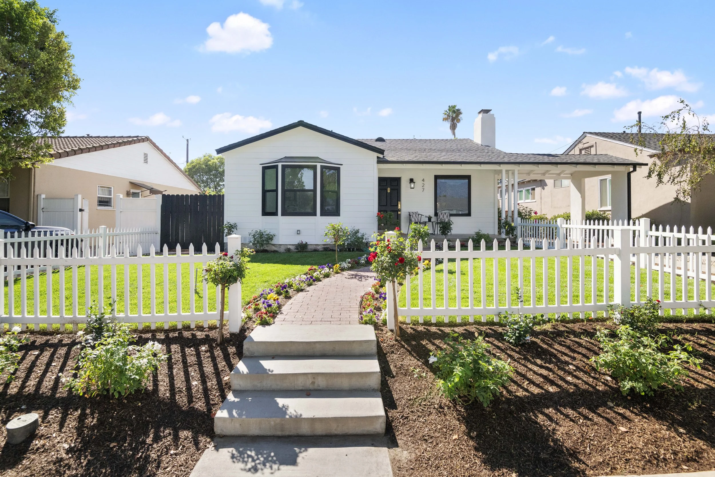 Charming Los Angeles home with black door, picket fence, and colorful garden — staged listing photo by Intuition Real Estate Photography & Imaging.