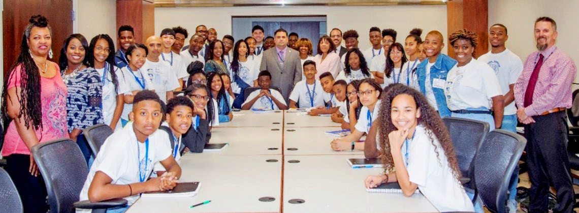 Large group of students and teachers gathered around a conference table in a classroom.