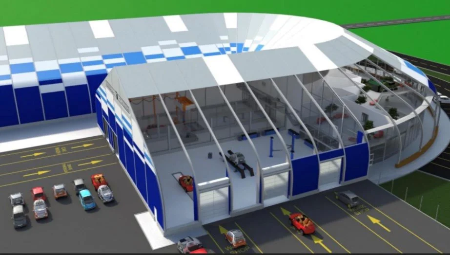 A modern indoor car showroom with a curved glass exterior, showcasing several cars parked in designated lanes, and a large structure featuring cars and possibly service or display areas inside.