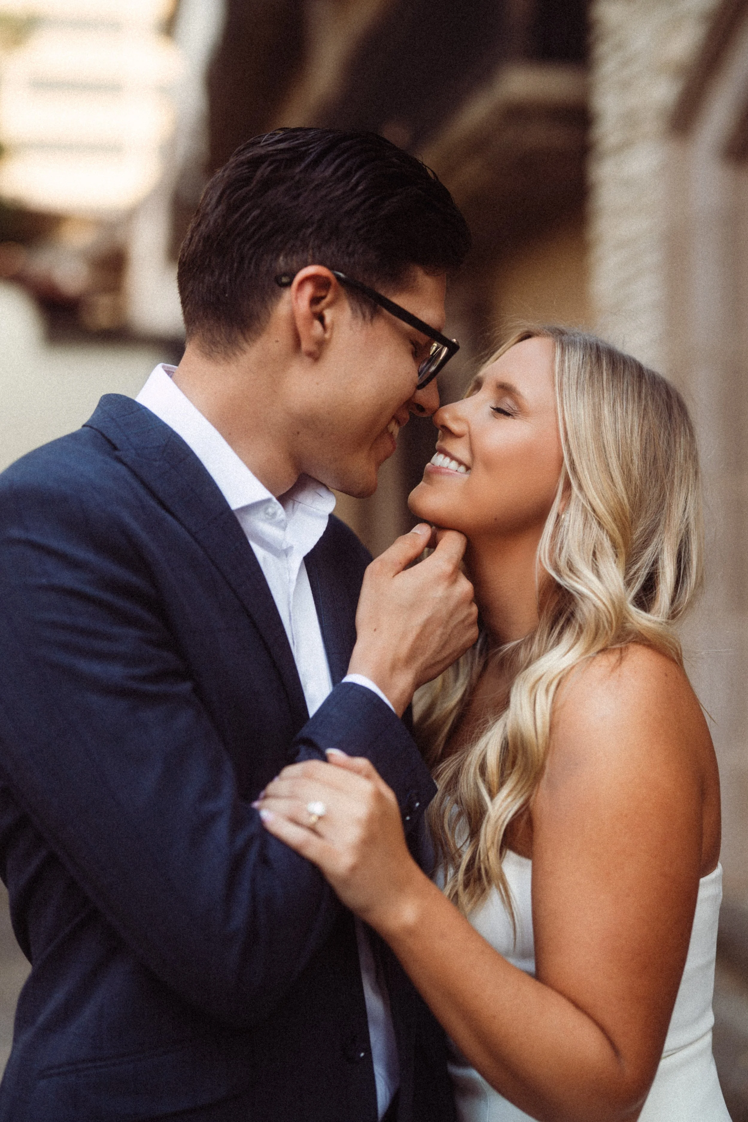  A warm, intimate engagement portrait of Alaina and Andres sharing a joyful, candid moment during their romantic session at the Mandalay Canal in Irving, Texas. The close-up shot highlights the stunning diamond engagement ring on her finger as she ho