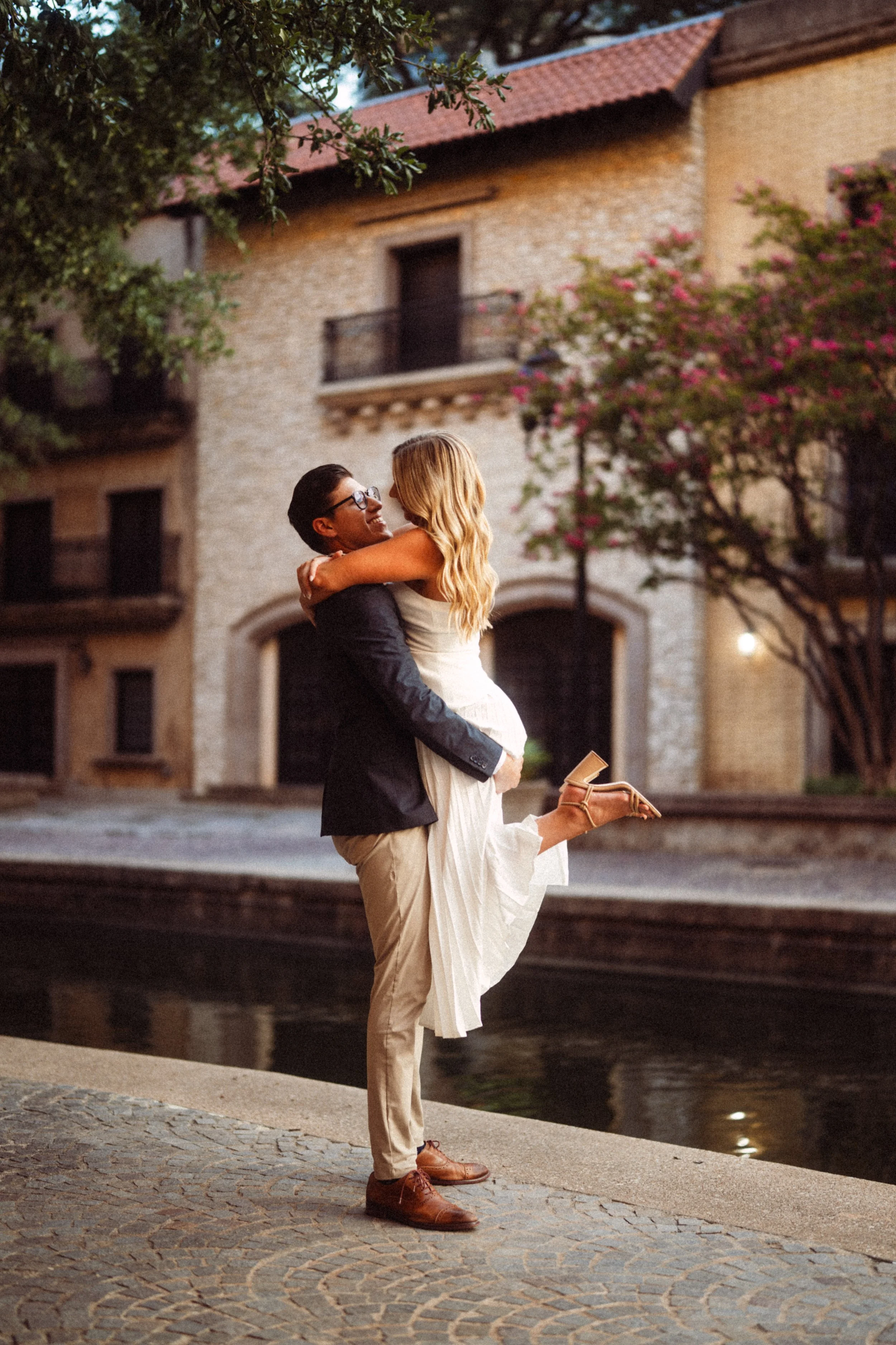  A timeless  engagement portrait  of Andres and Alaina at the  Mandalay Canal in Irving, Texas . This romantic shot captures a joyful  lift pose  on the  cobblestone walkways  overlooking the water. Featuring  European-style architecture  and elegant