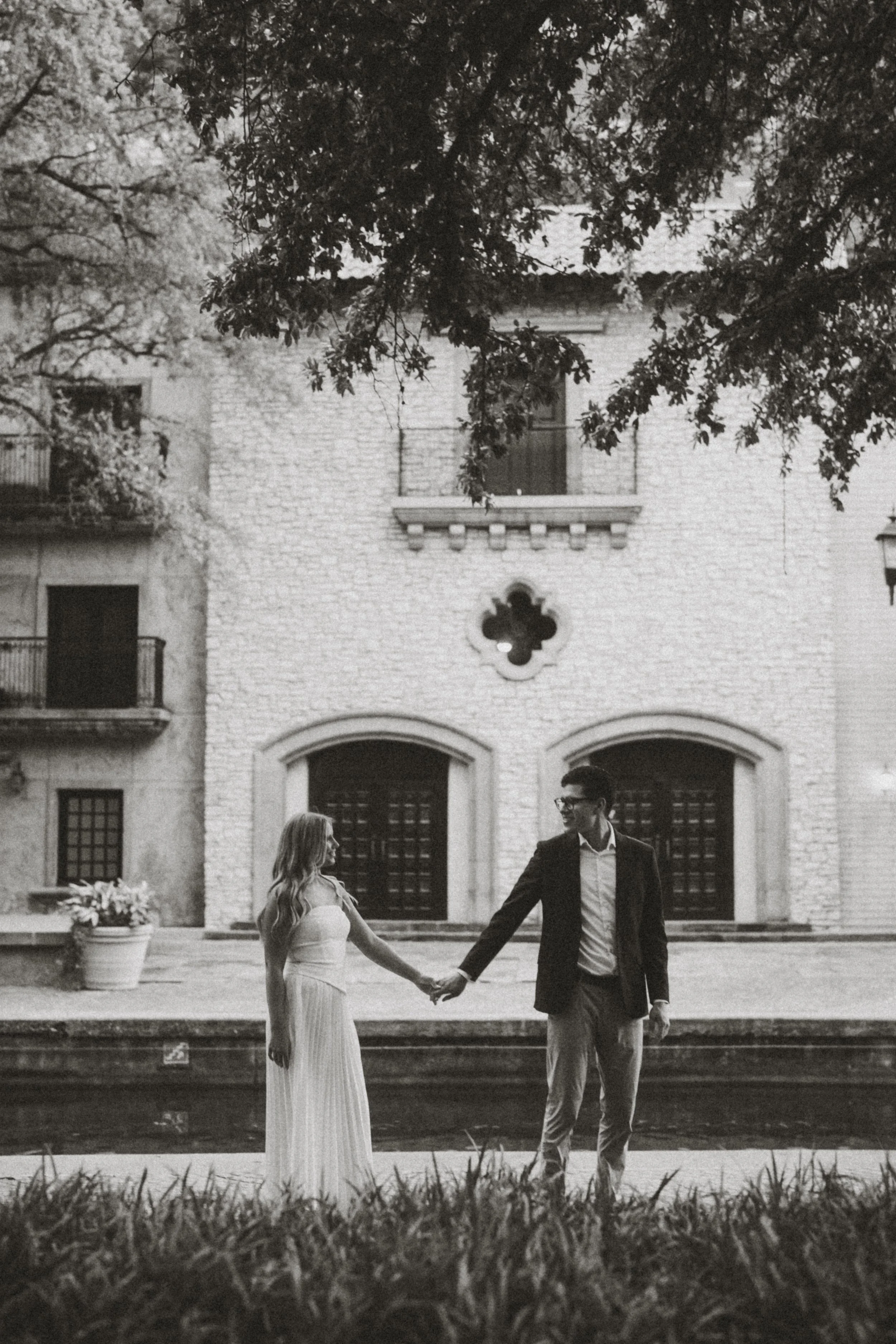  A classic  black and white engagement photograph  of Andres and Alaina holding hands along the  Mandalay Canal in Las Colinas . This romantic, wide-angle shot highlights the stunning  European-style stone architecture  along the water, offering a ti