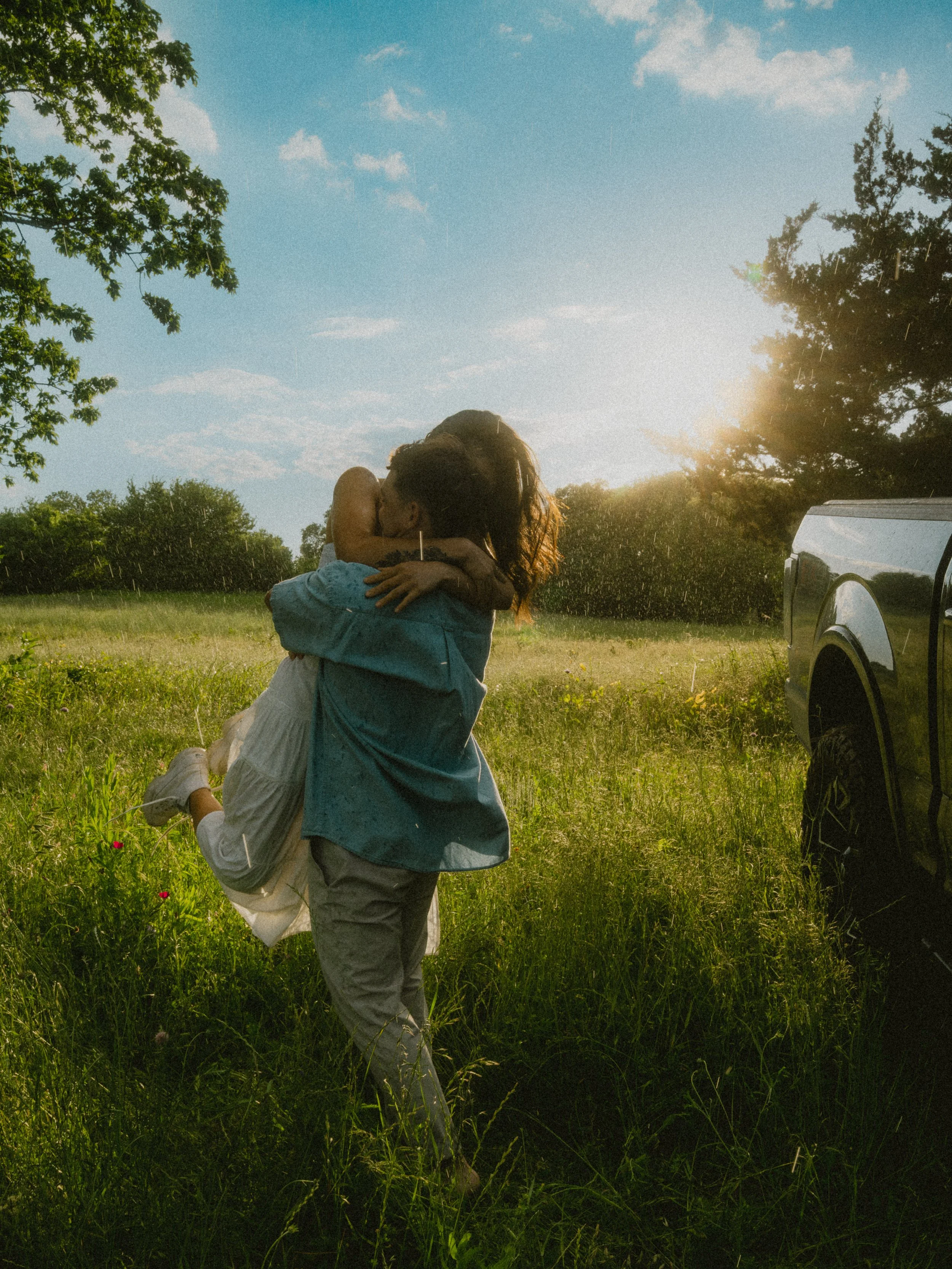  Candid couple hugging in a sun-drenched field during a sunshower at  Erwin Park in McKinney , Texas. 