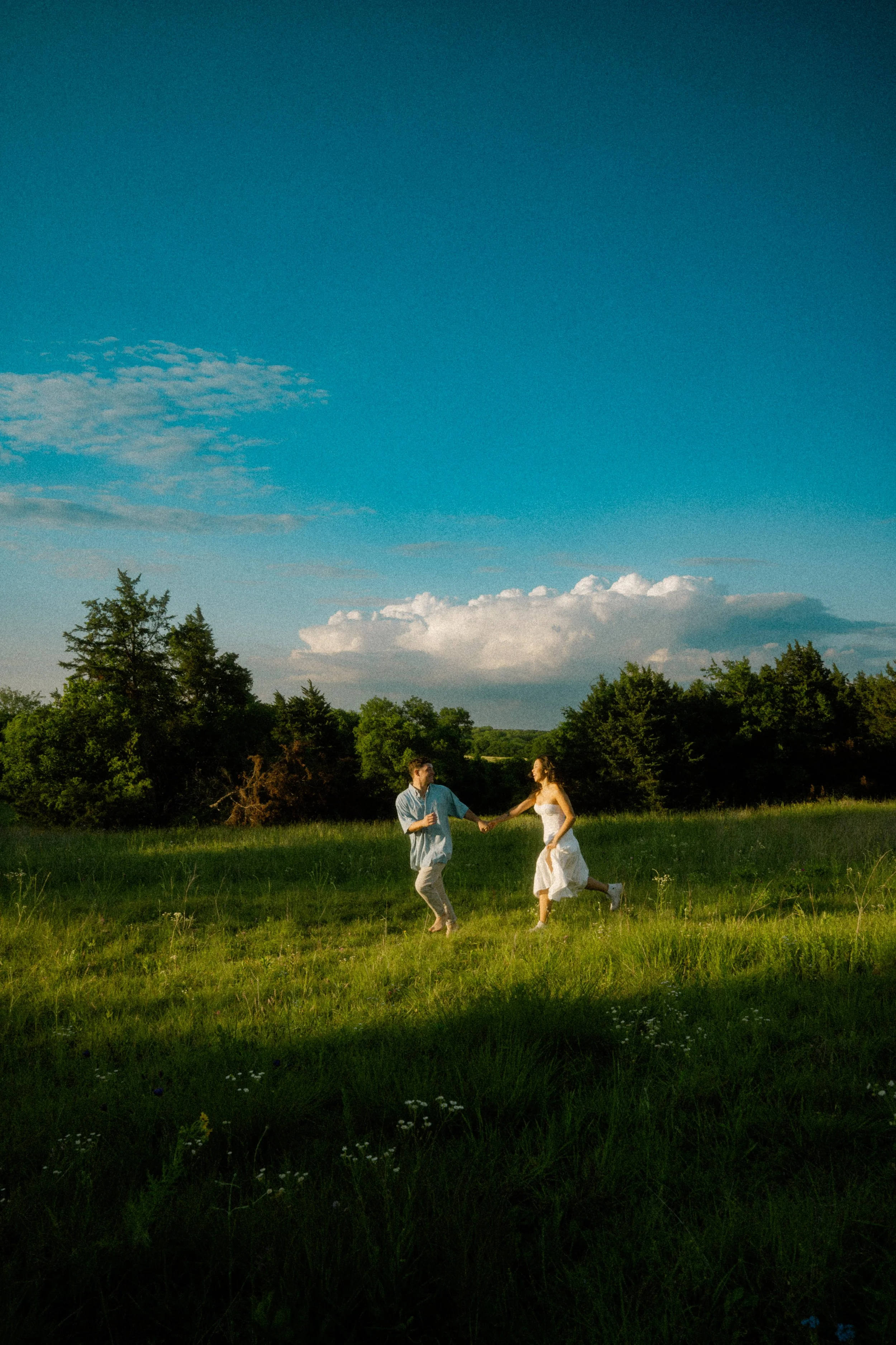  Cinematic wide shot of a couple running through a grassy field at  Erwin Park in McKinney , TX, during golden hour. 
