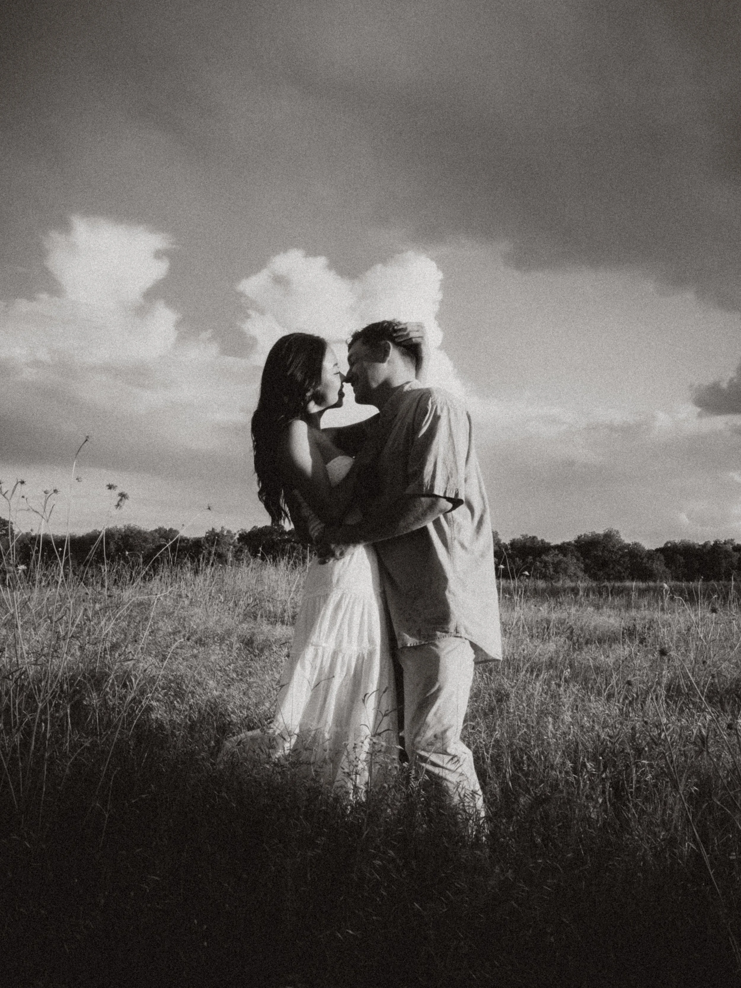  Black and white film-inspired portrait of a couple embracing in a meadow under storm clouds at  Erwin Park in McKinney . 