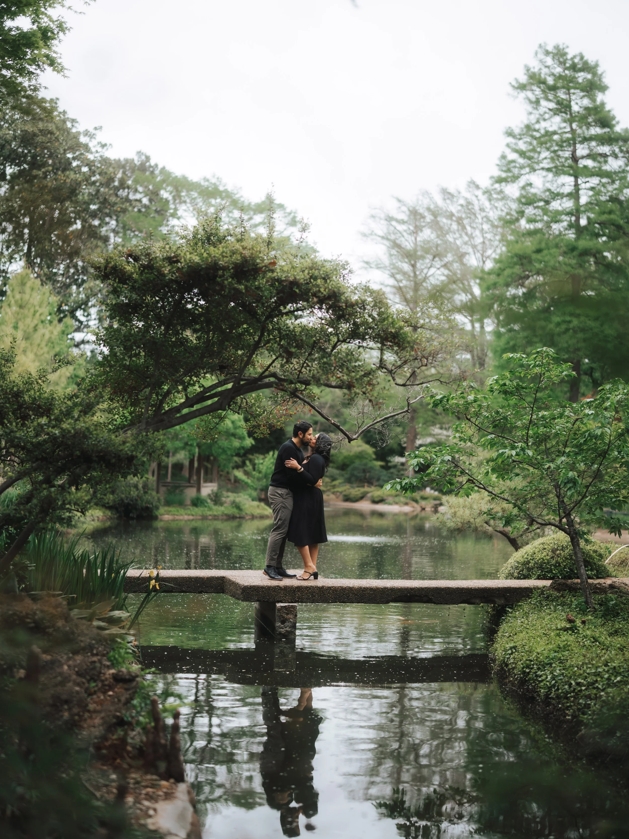  Couple kissing on a stone bridge with water reflections at the Fort Worth Botanic Garden Japanese Garden. 