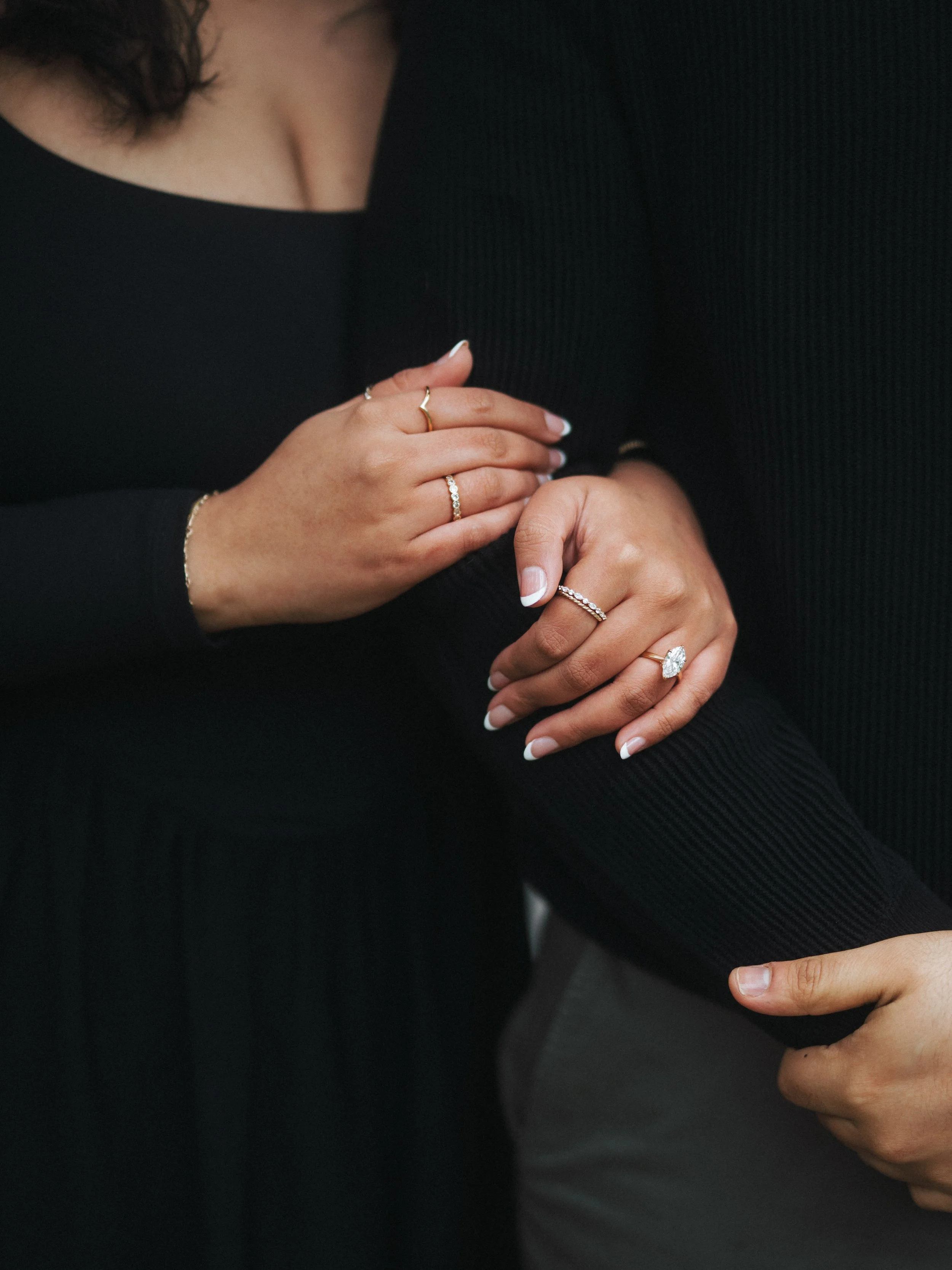  Detail shot of a woman's hand featuring a marquise diamond engagement ring and gold jewelry during a proposal. 