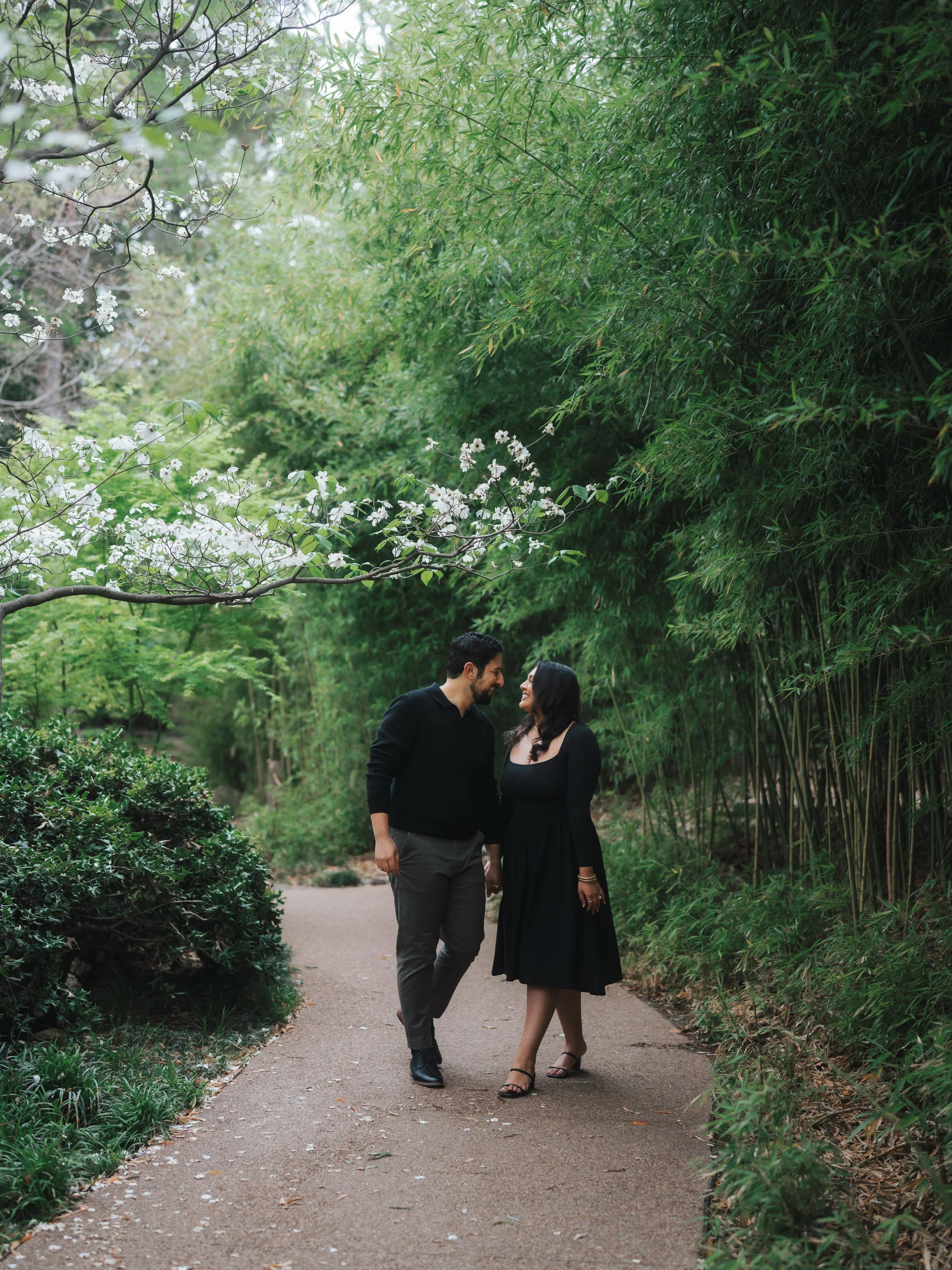  Couple walking through a bamboo forest and white spring blossoms at the Fort Worth Botanic Garden. 