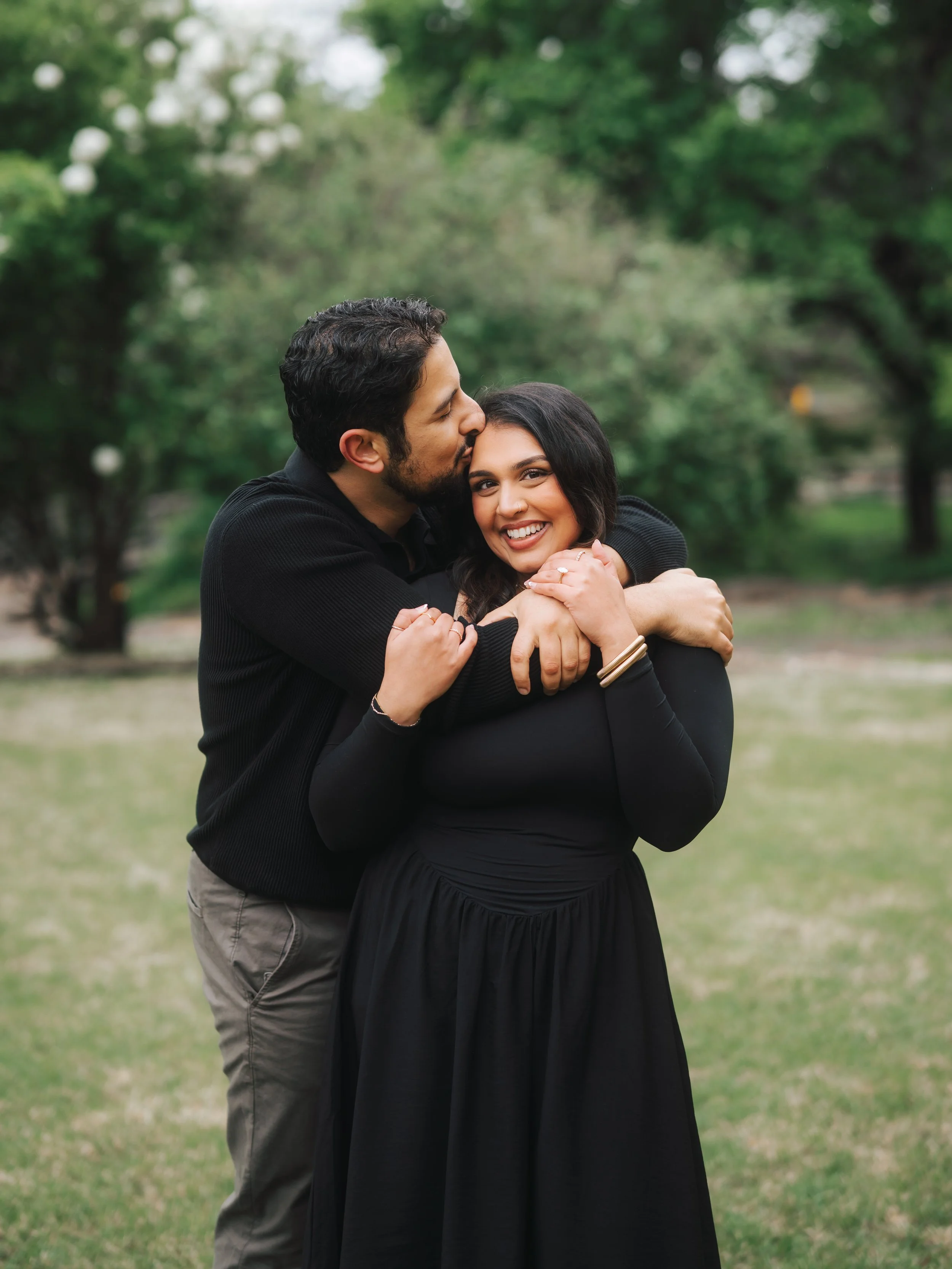  Groom-to-be kissing his fiancée's forehead during a spring engagement session at the Fort Worth Botanical Gardens. 