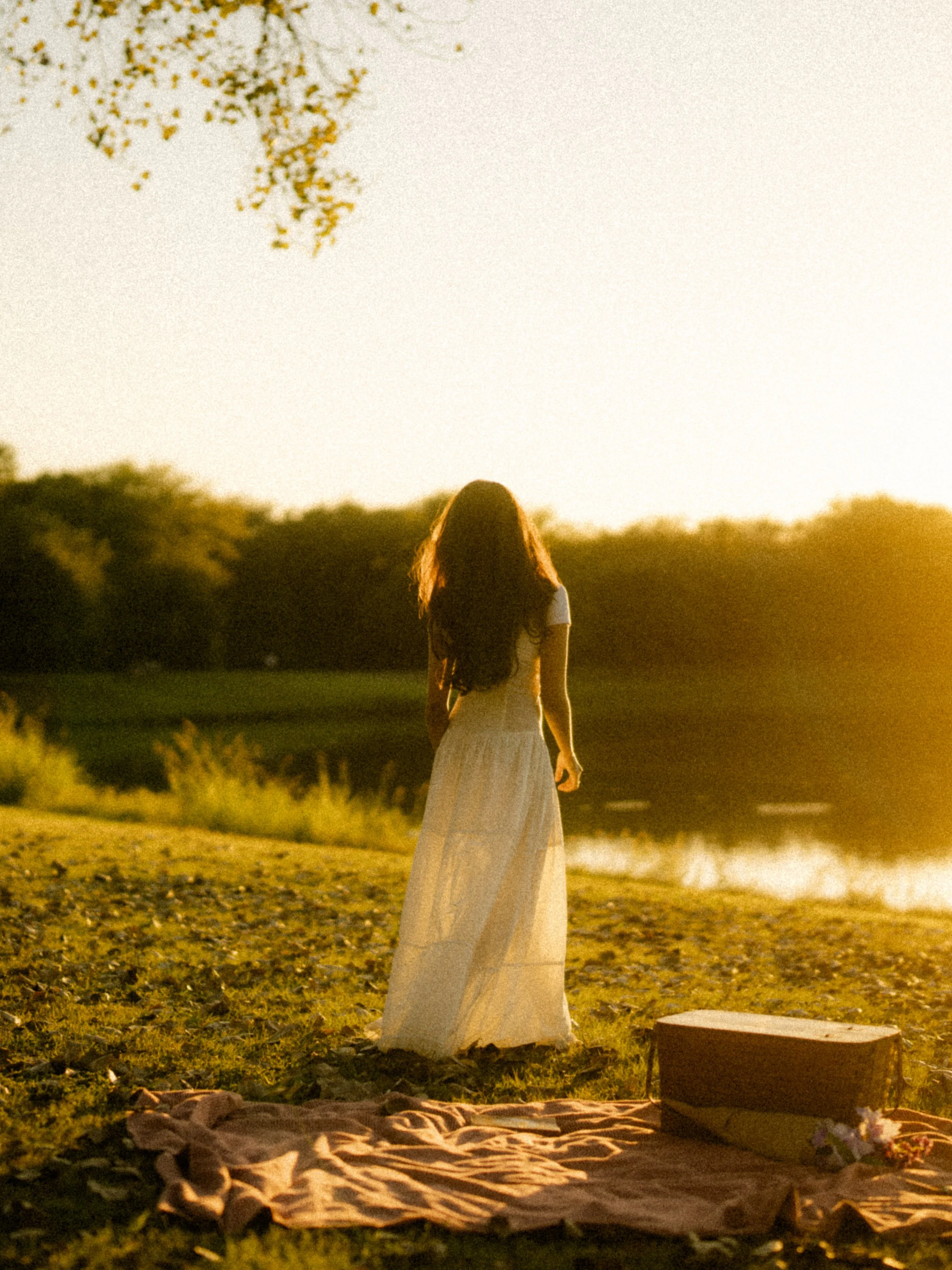  Ethereal back view of a woman in a white dress walking through a field towards a sunset lake at Breckinridge Park. Cinematic film grain. 