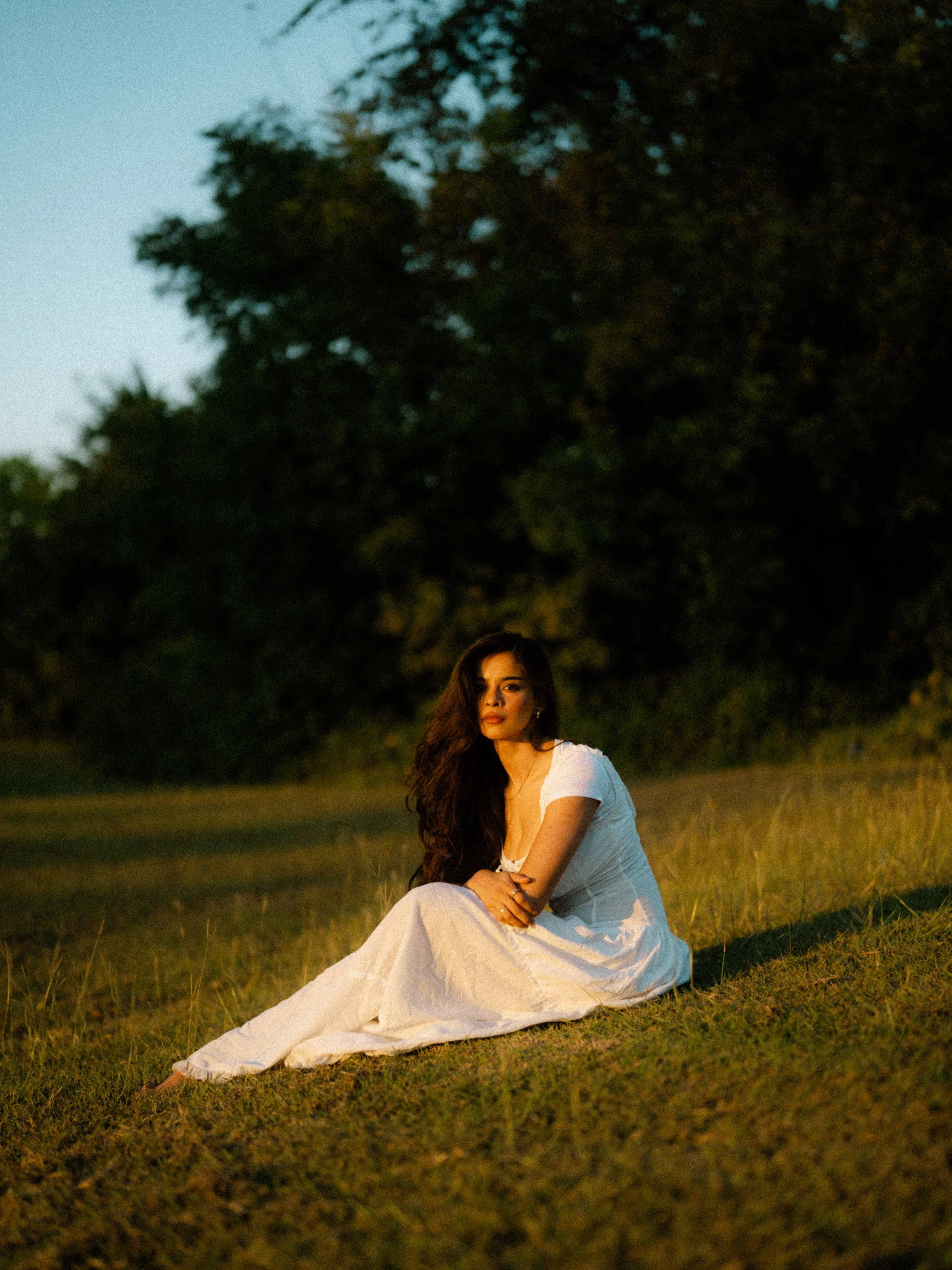  Pensive film portrait of model Riya sitting side-profile in a grassy field during autumn in Richardson, TX. Cinematic golden hour mood. 