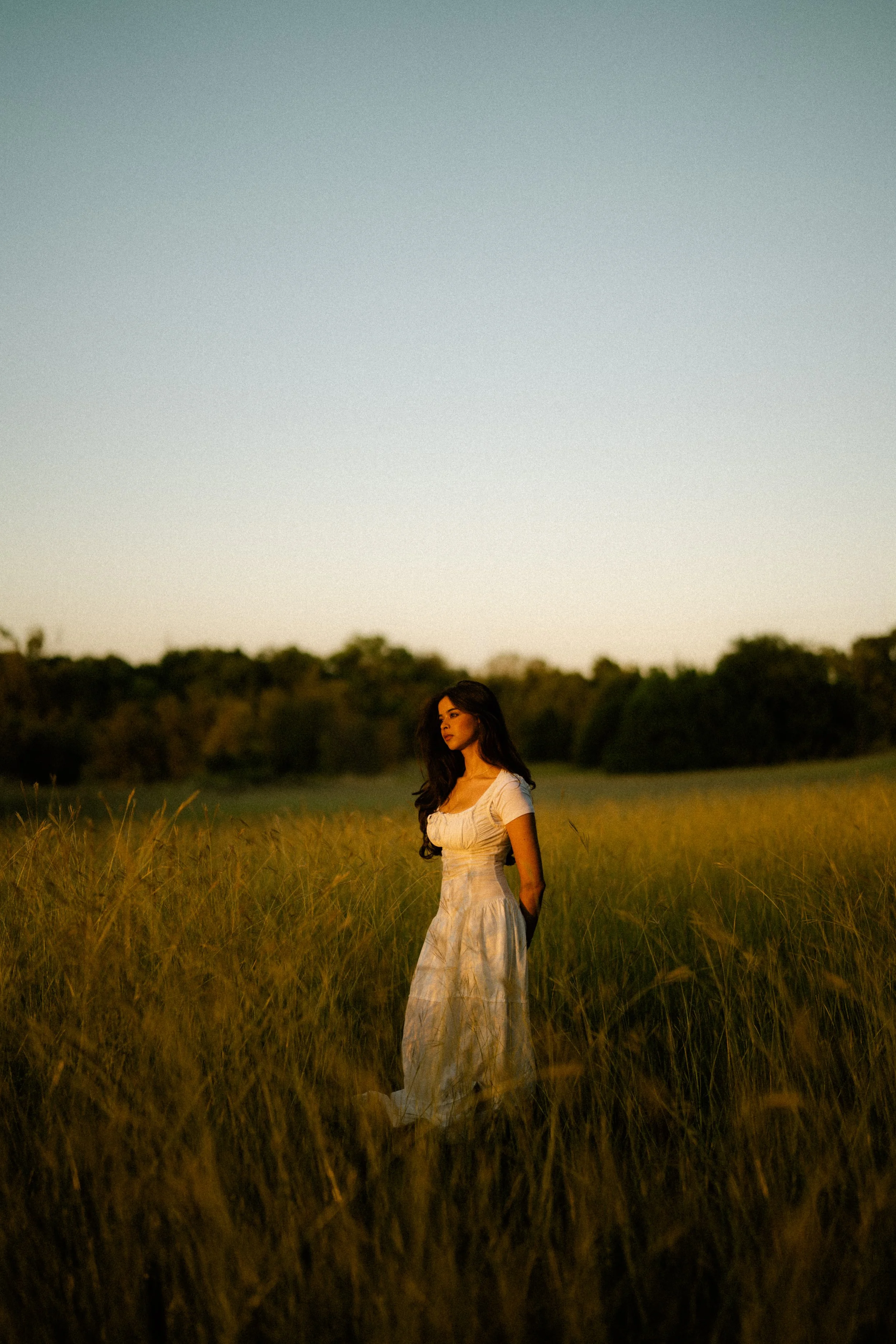  Cinematic full-body shot of Riya standing in tall golden grass during sunset. Film photography aesthetic at Breckinridge Park in the Dallas area. 