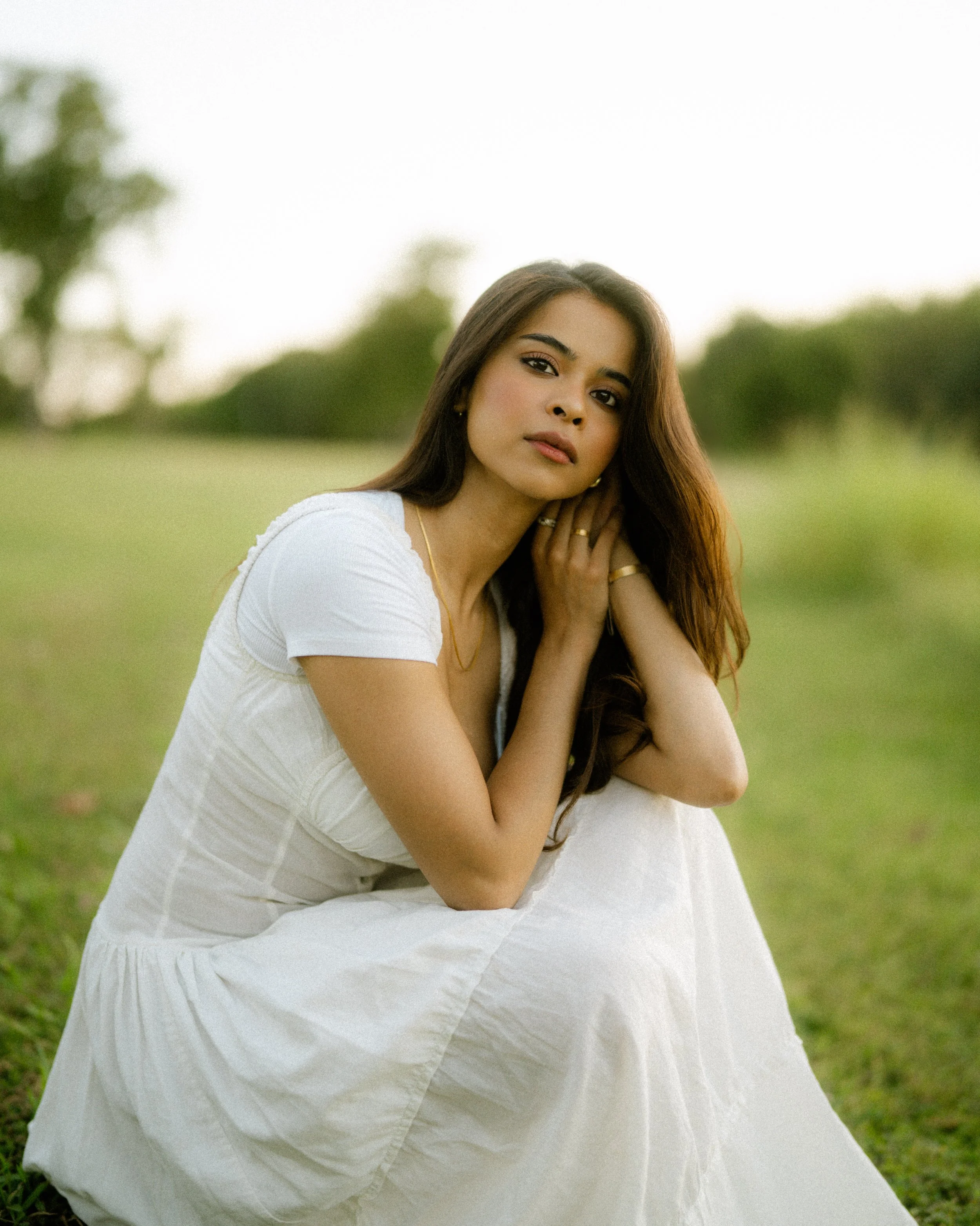  Cinematic portrait of Riya sitting on a grassy slope during sunset. Warm side lighting and film grain aesthetic at Breckinridge Park. 