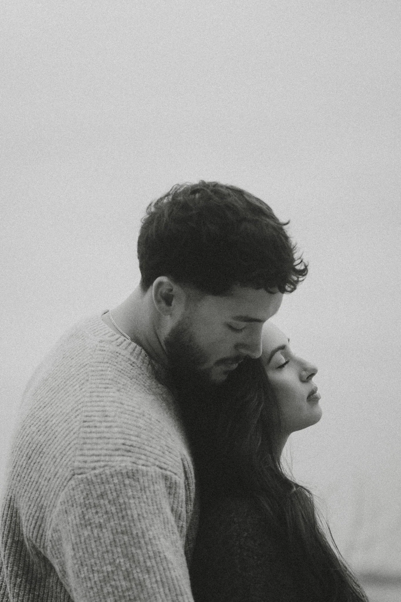 A black and white photo of a couple holding hands and running through a grassy field during sunset or sunrise.