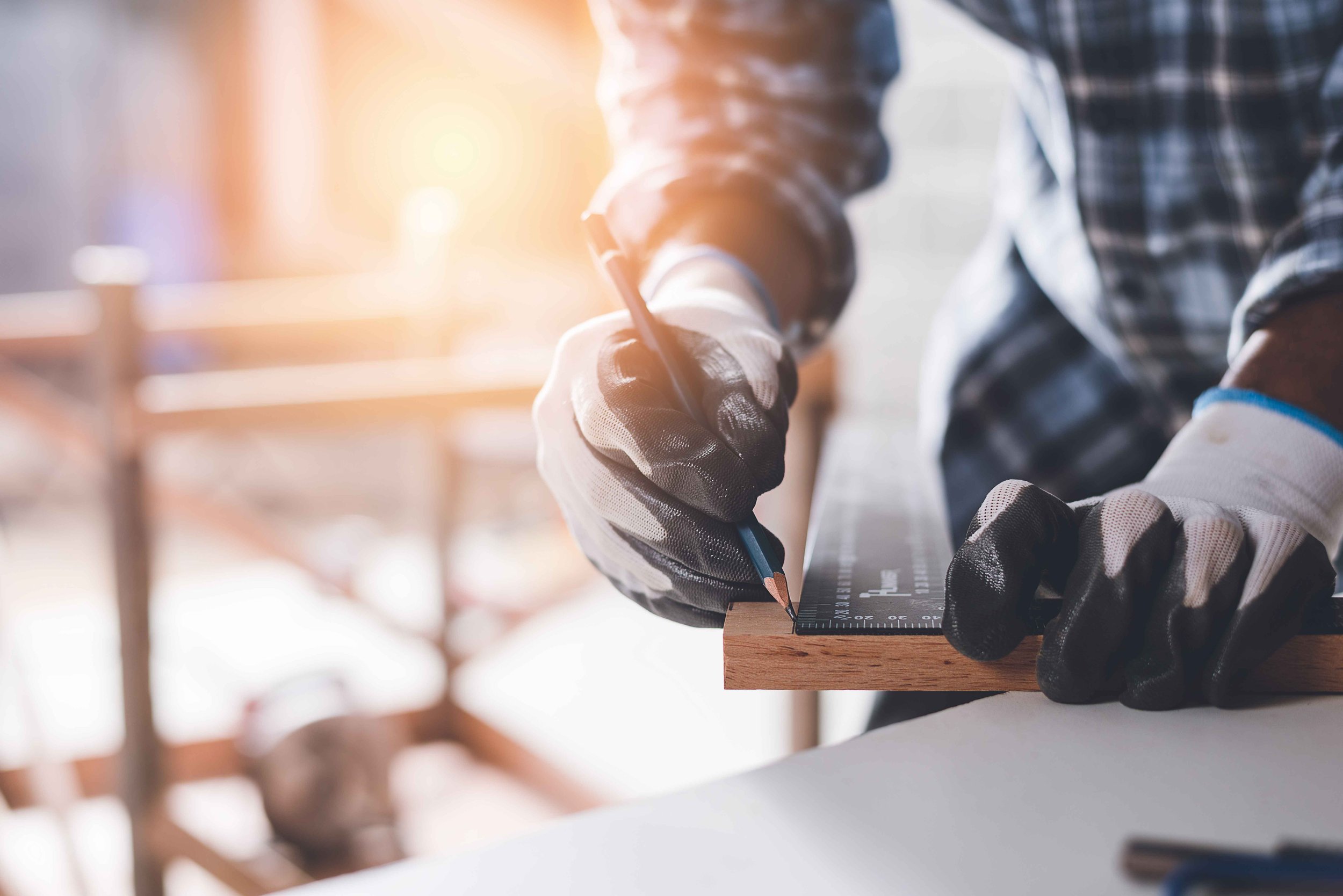 A person measuring a piece of wood with a black ruler in a woodworking or carpentry workshop.