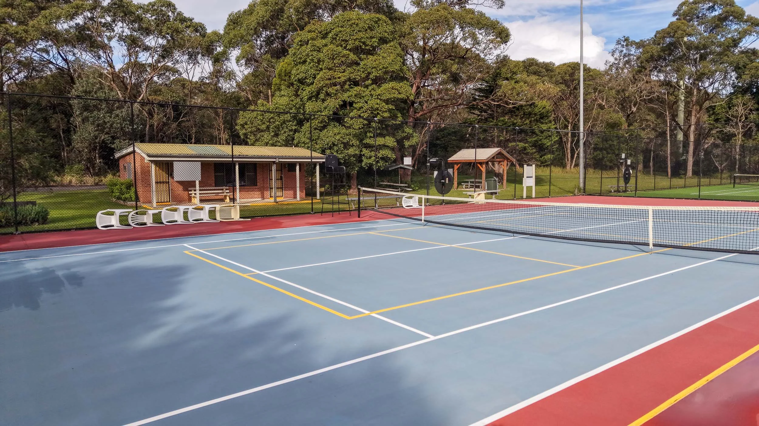 A view from the tennis courts looking toward the brick clubhouse building, which features a covered veranda and seating area.
