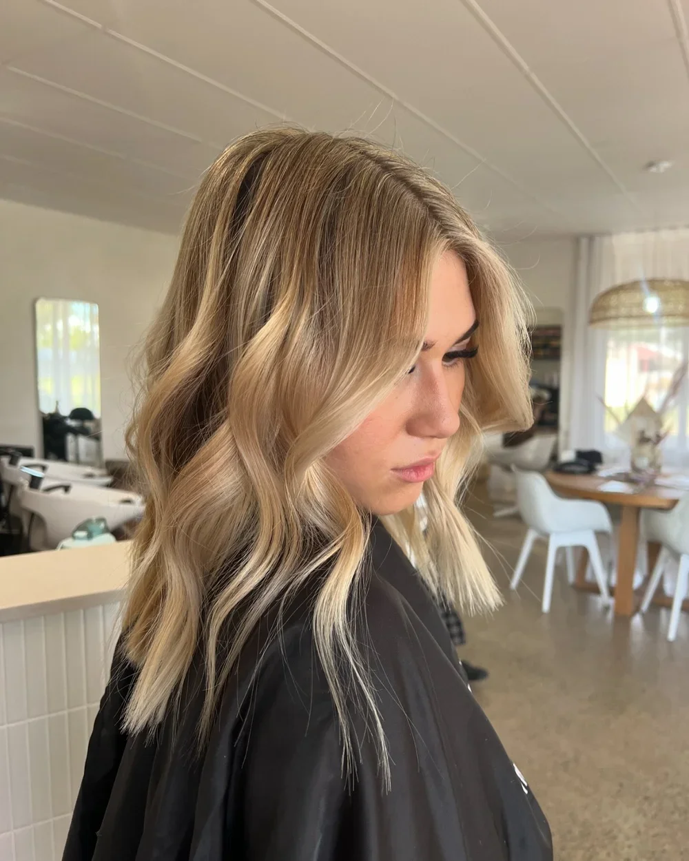 Client showcasing soft blonde wavy hair styling inside the bright Silk and Stone Studio hair salon.