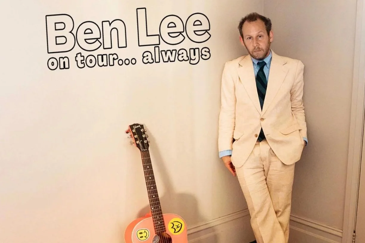 Ben Lee standing against a wall beside a sticker-covered acoustic guitar, next to text reading 'Ben Lee on tour… always