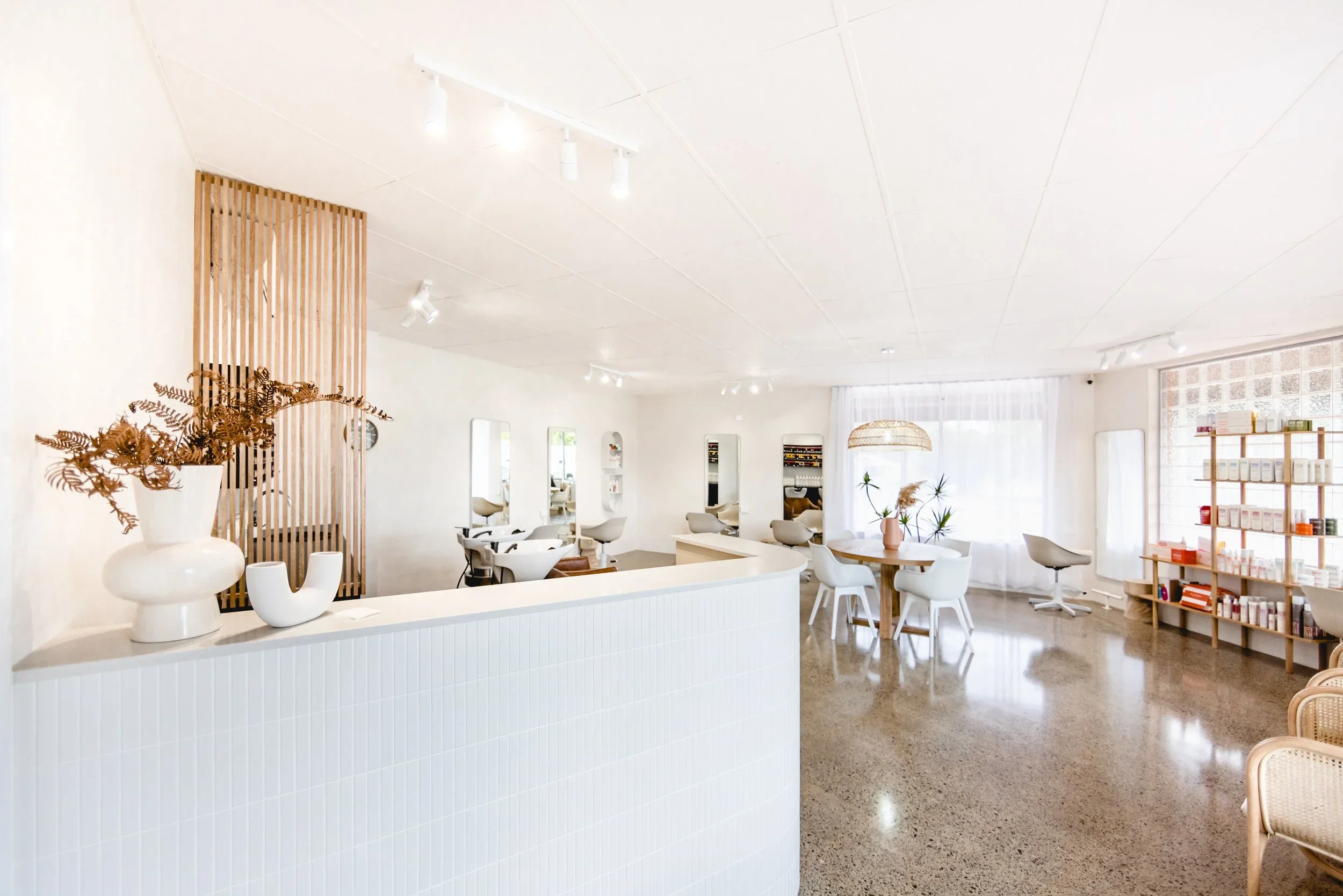 Bright aesthetic interior of Silk and Stone Studio hair salon featuring white styling stations, timber accents, and retail shelving.