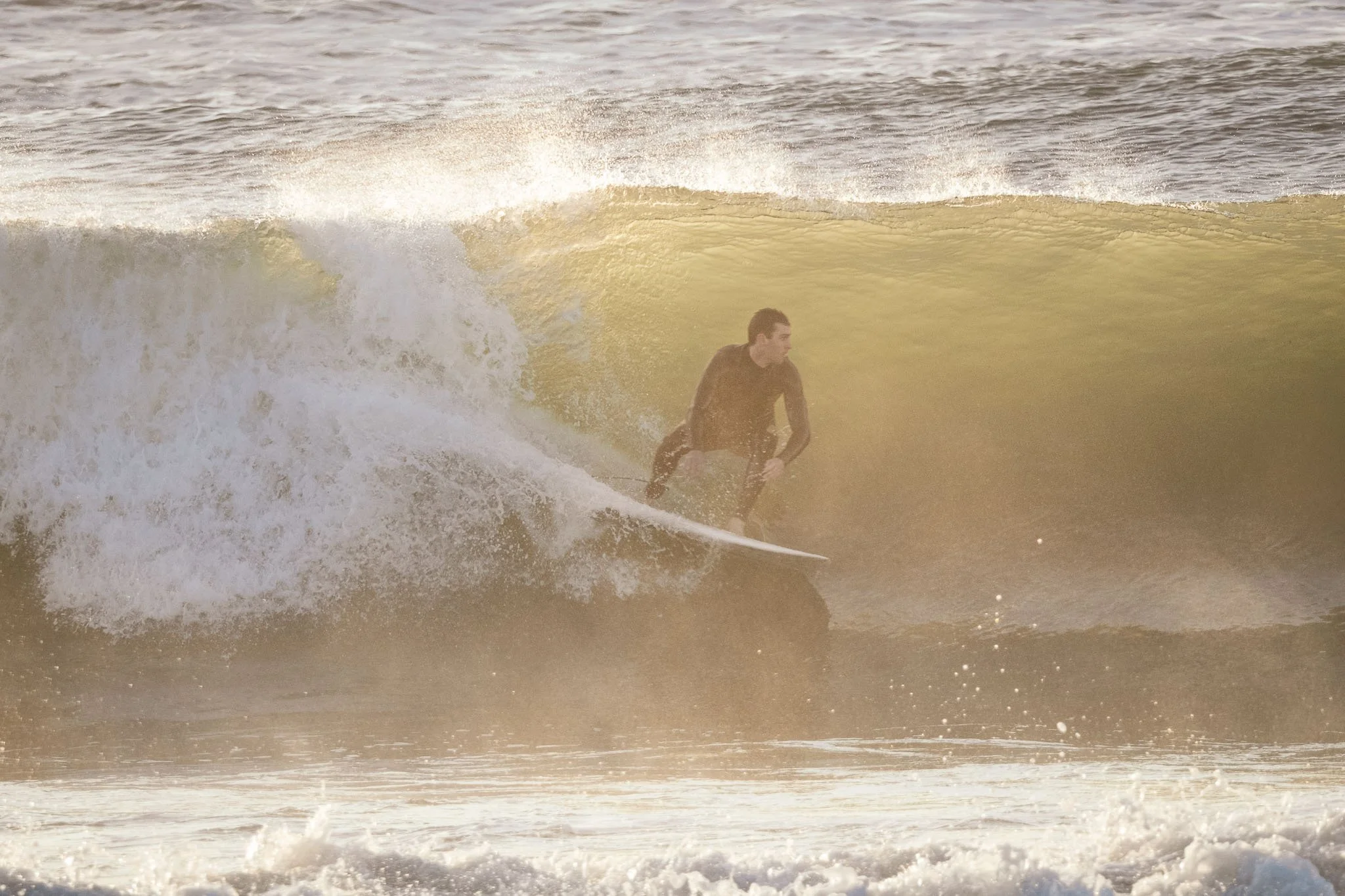 A male surfer riding a wave in the ocean at Shoalhaven Heads during sunrise.