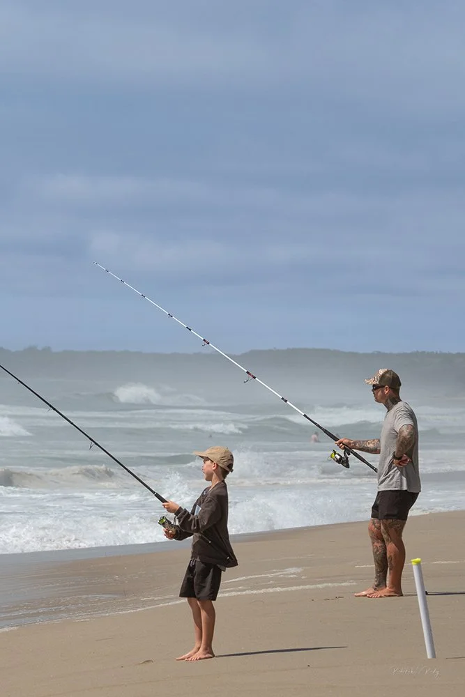 A father teaching his young son how to surf fish with long rods on Seven Mile Beach at Shoalhaven Heads.