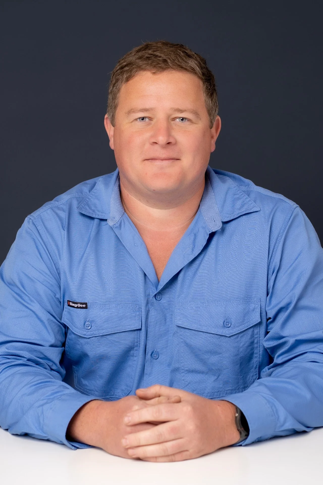 Professional headshot of Keith, the owner of Coast Flow, wearing a blue long-sleeve work shirt against a dark studio background.