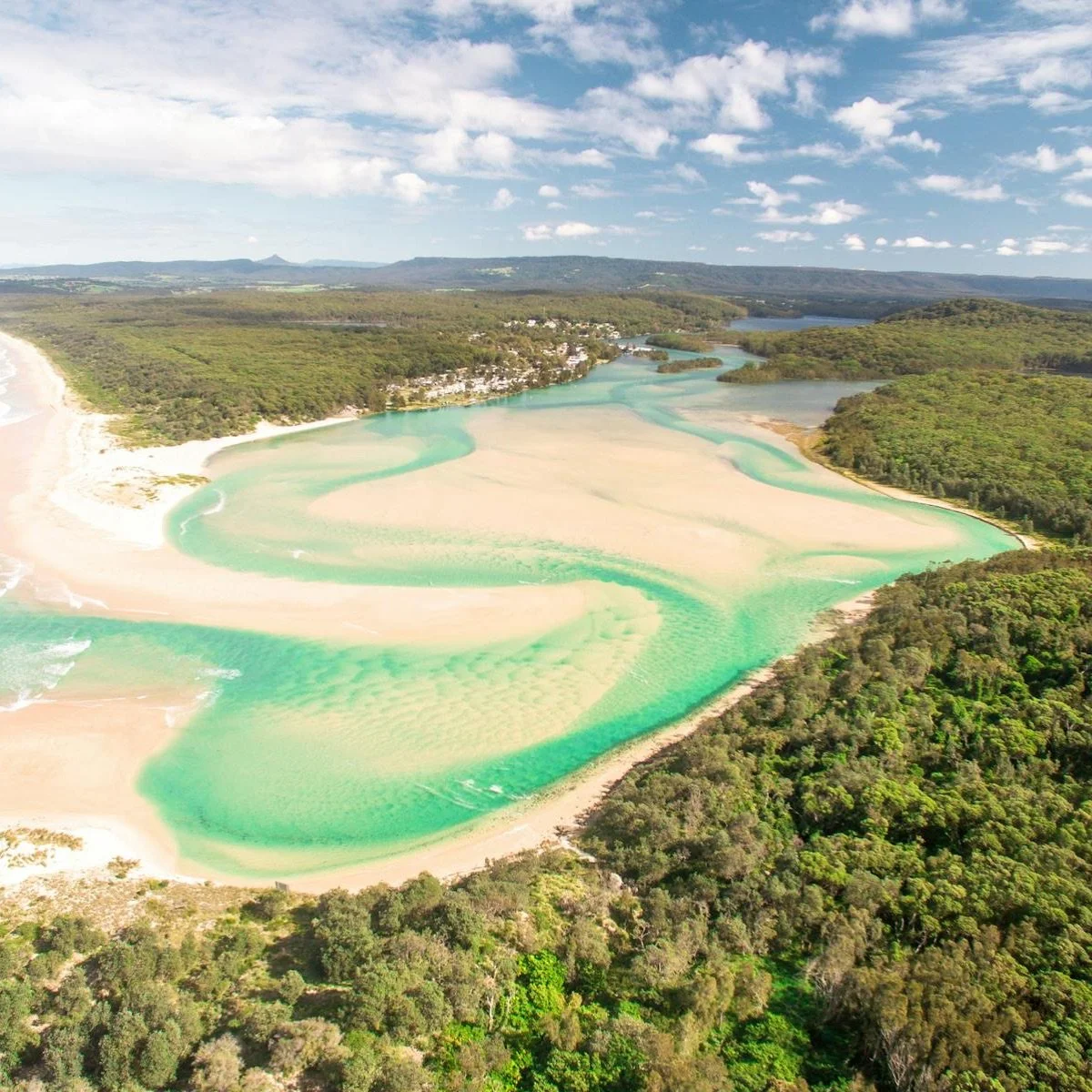 Aerial view of the turquoise estuary and sandy shoals of Lake Conjola meeting the ocean along the South Coast of NSW.