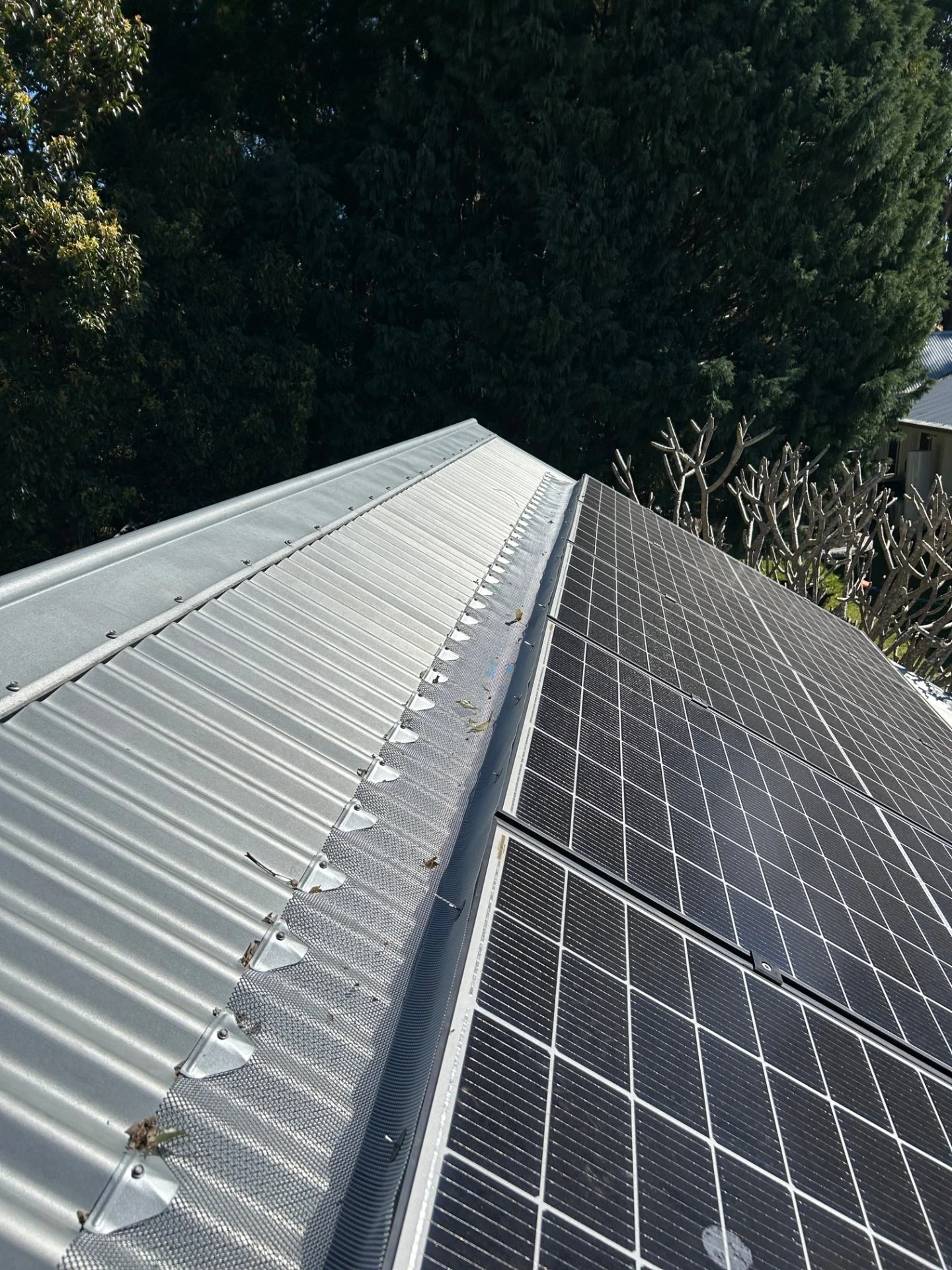 Durable solar panel mesh installed along the base of solar panels on a silver corrugated metal roof to prevent birds and possums from nesting underneath.