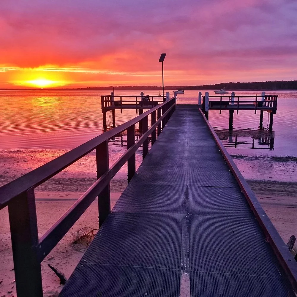 A vibrant purple and orange sunset over the water looking down the long jetty at Carters Corner, Shoalhaven Heads