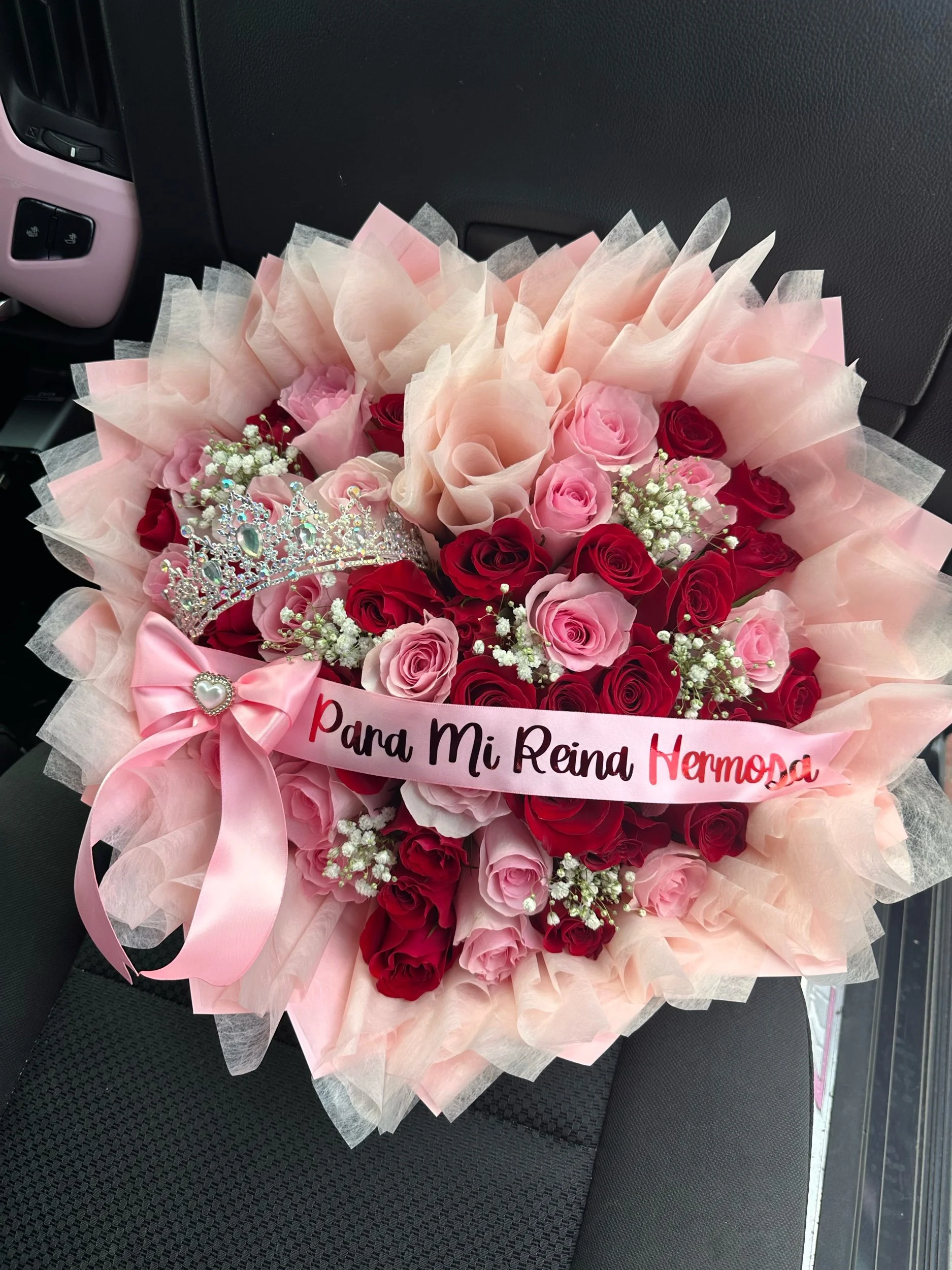 Red and pink rose bouquet with baby’s breath clusters, a message banner, crown, and pink floral wrapping.