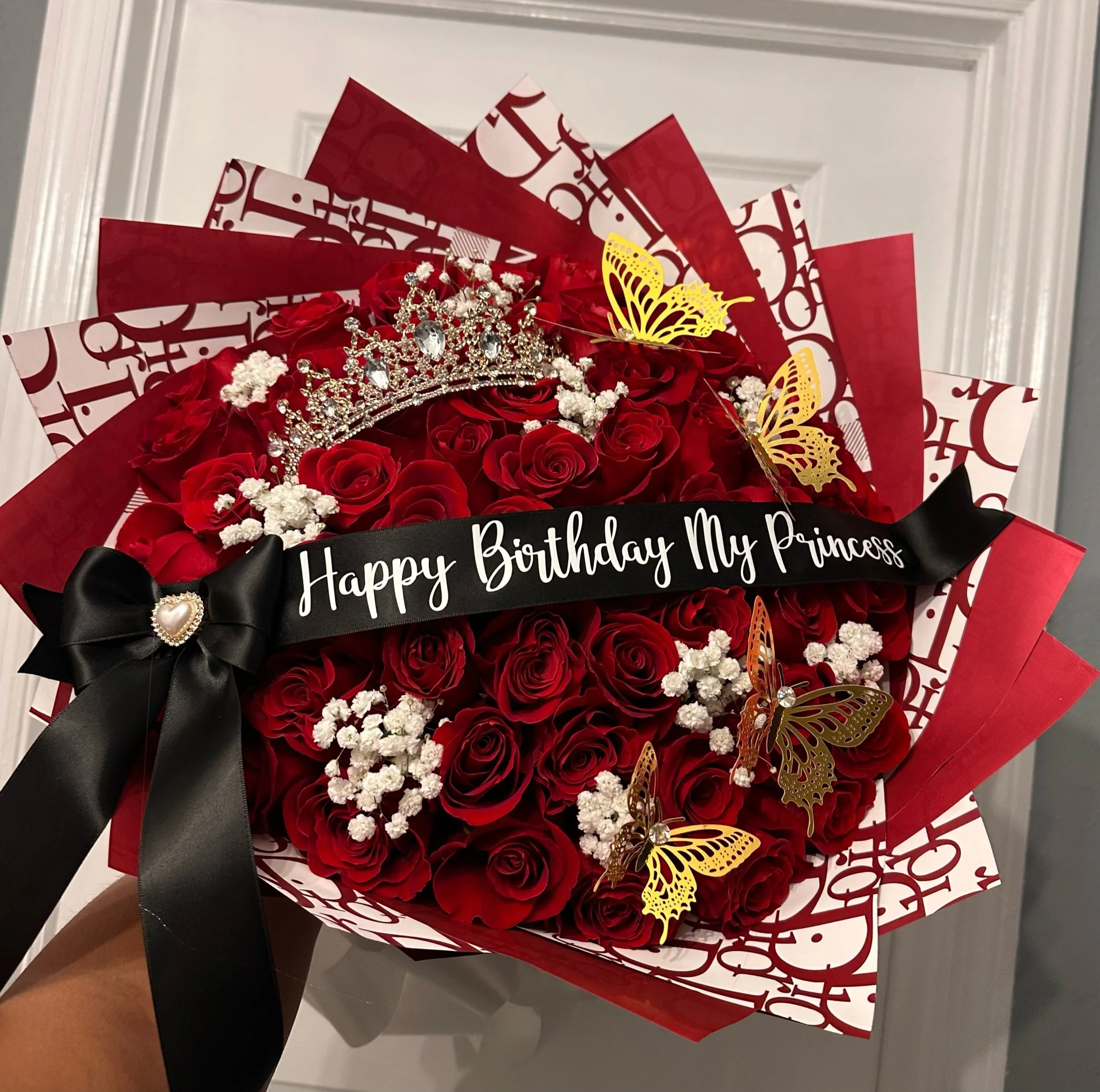 Red rose bouquet with gold butterflies, a gold tiara, message banner, and luxury designer-patterned floral wrapping.