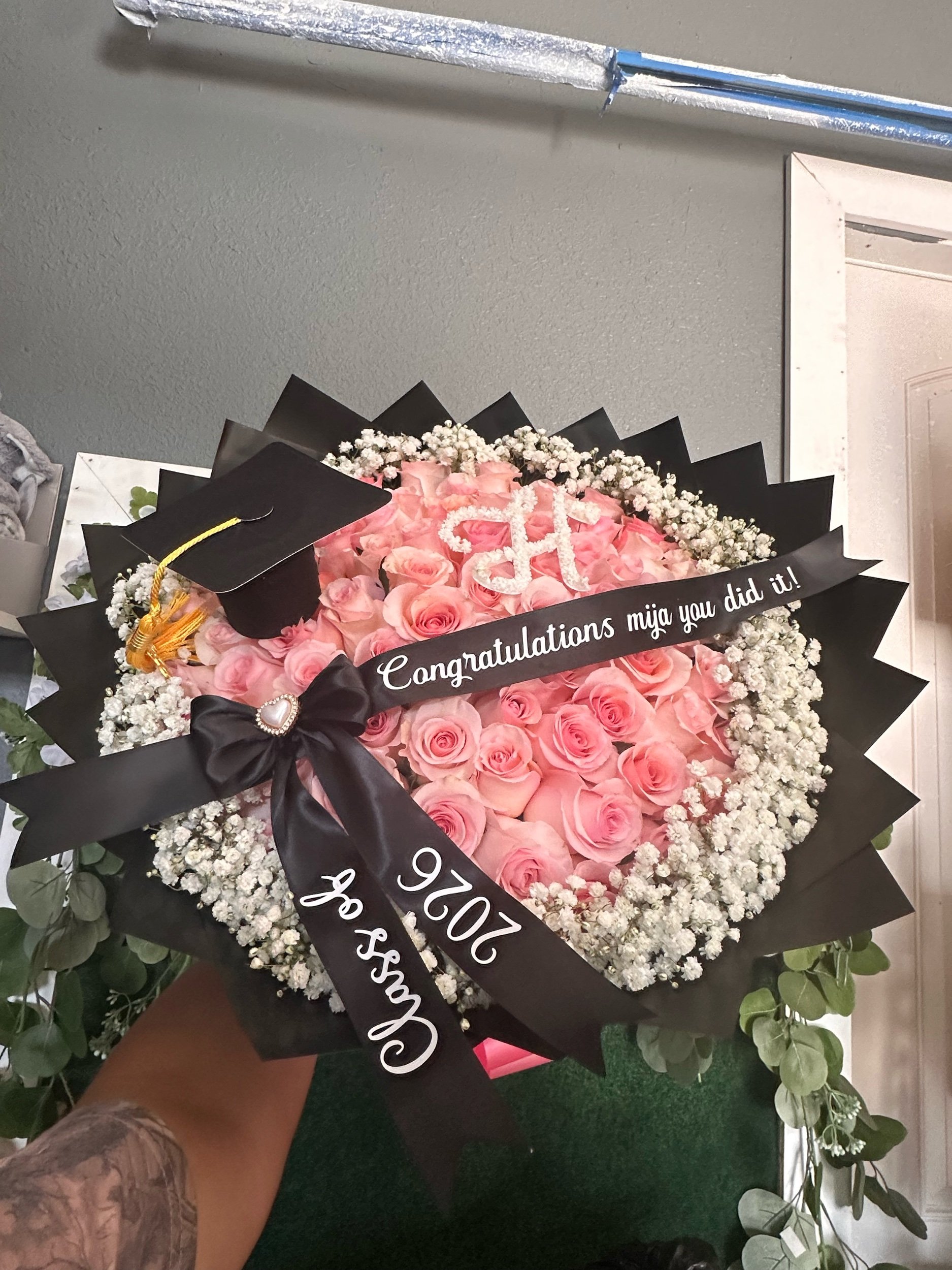Pink rose graduation bouquet with a baby’s breath border, personalized baby’s breath letter, message bow, and graduation cap.