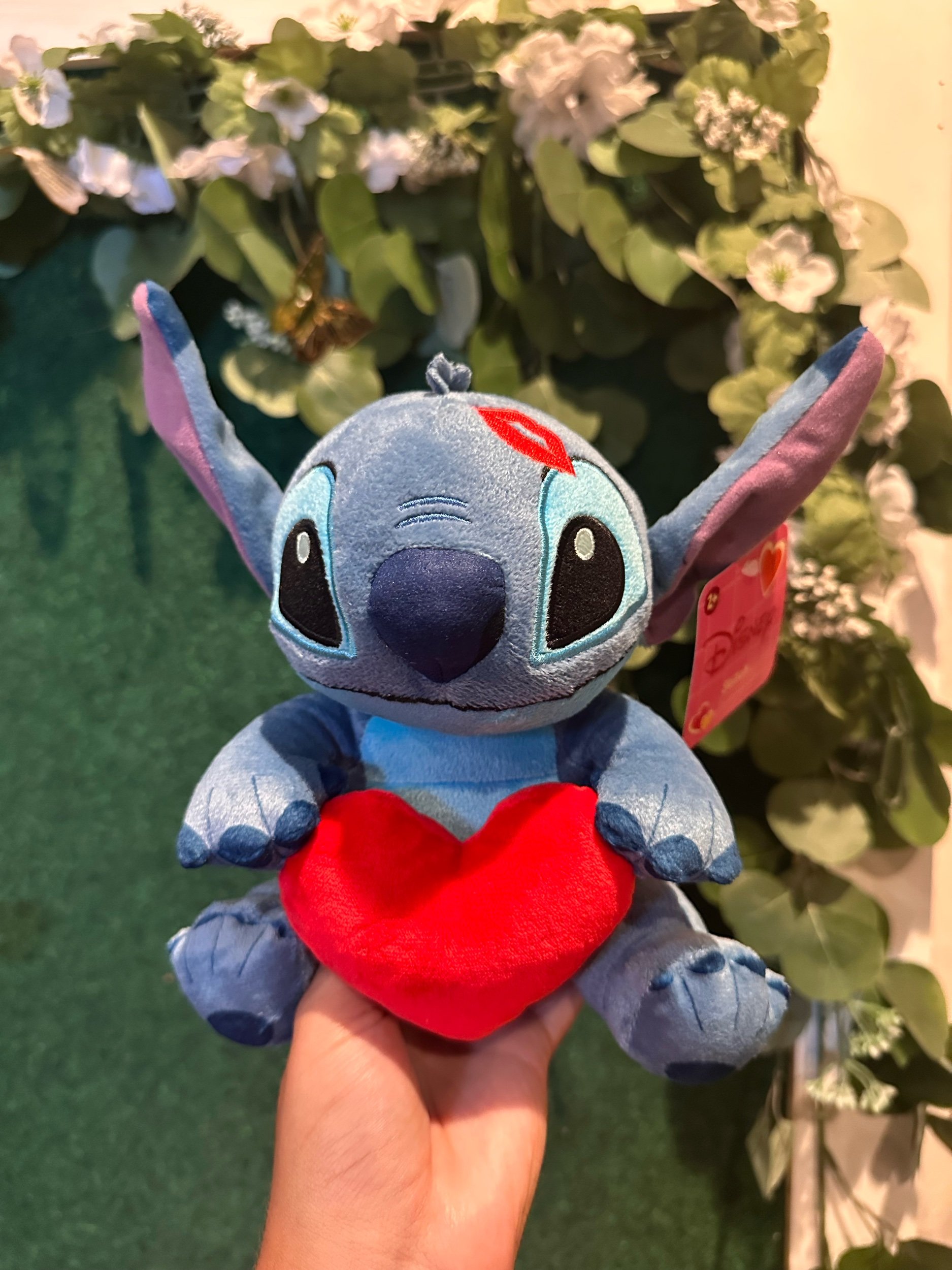 Blue Stitch plush toy with large ears, and embroidered kiss print on head. Stitch is also holding a heart.