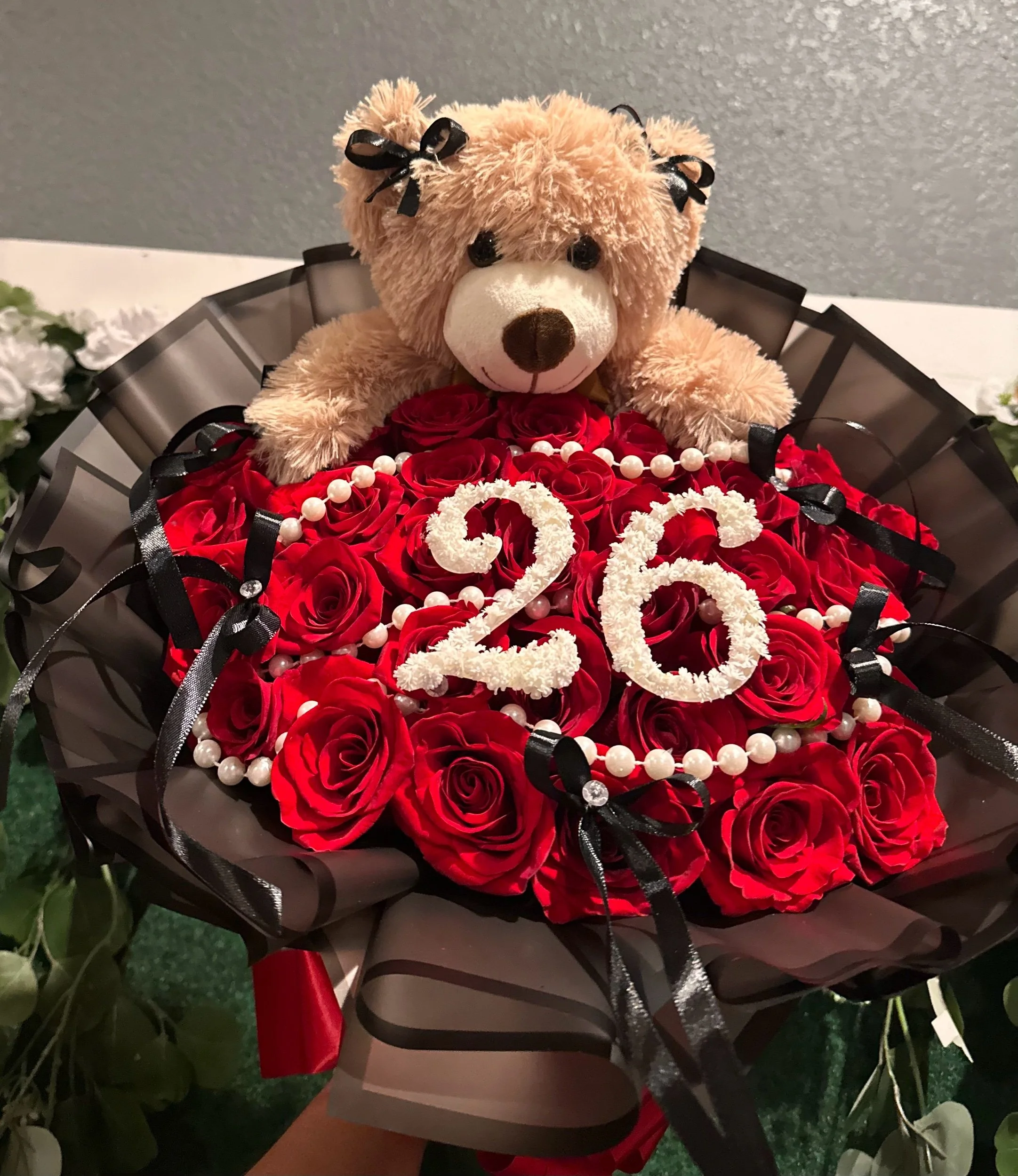 Red rose bouquet with pearl strands, long black bows, baby’s breath numbers, and a teddy bear.