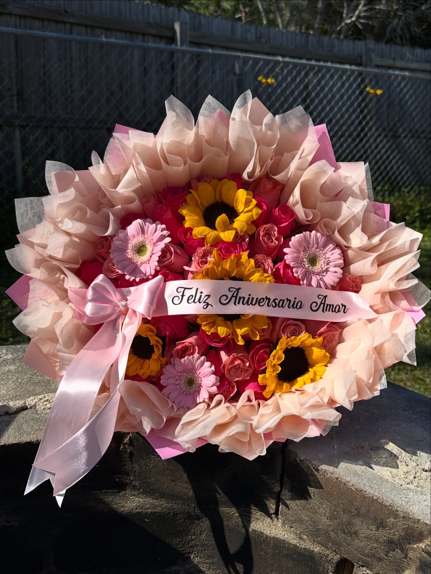 Pink and hot pink rose bouquet with sunflowers, gerbera daisies, a message banner, and layered tissue paper.