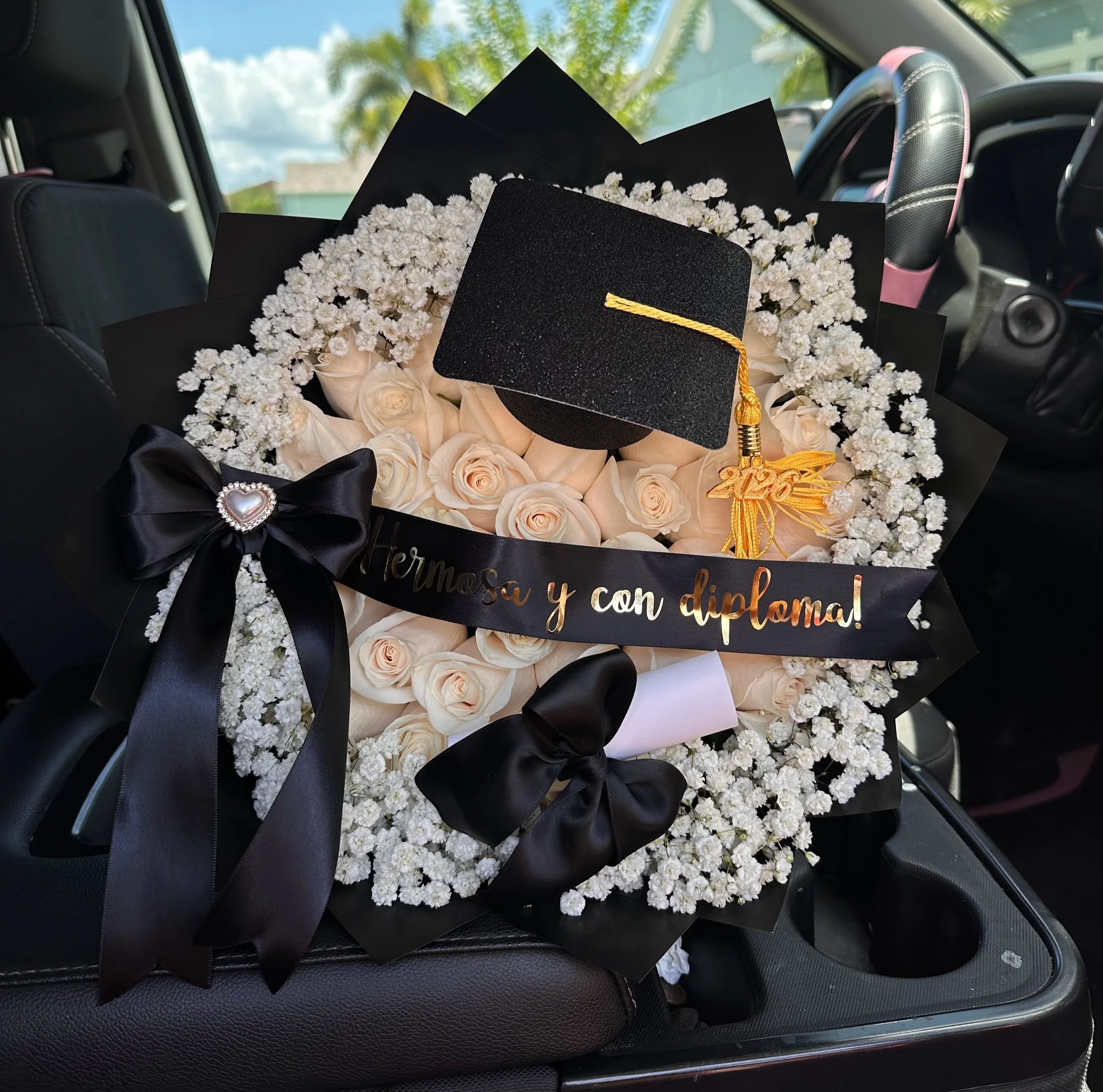White rose graduation bouquet with a baby’s breath border, message banner, diploma, and graduation cap accents.