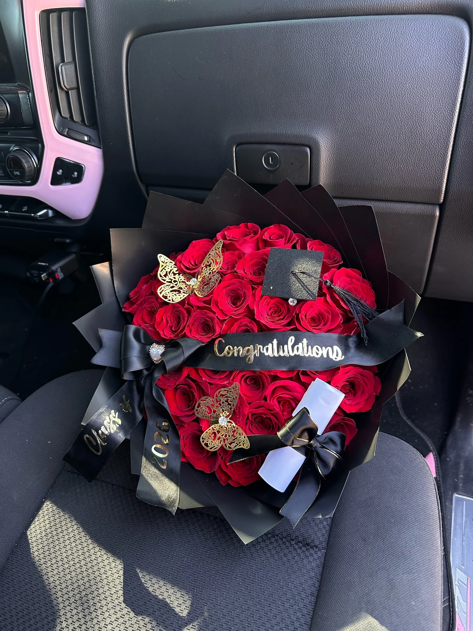 Red rose graduation bouquet with a message banner, diploma, graduation cap, and golden butterflies, wrapped in black floral paper.