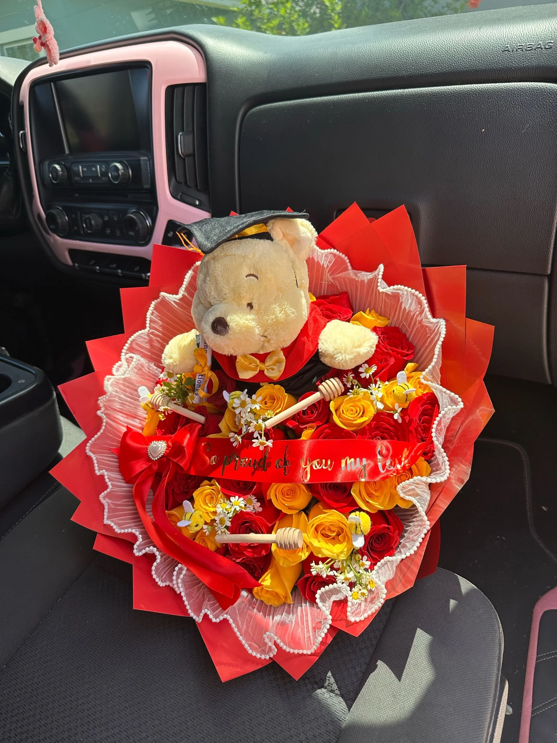 Yellow and red rose bouquet with chamomile, honey sticks, decorative bees, pearl mesh, and a Winnie the Pooh graduation plush, wrapped in red floral paper.