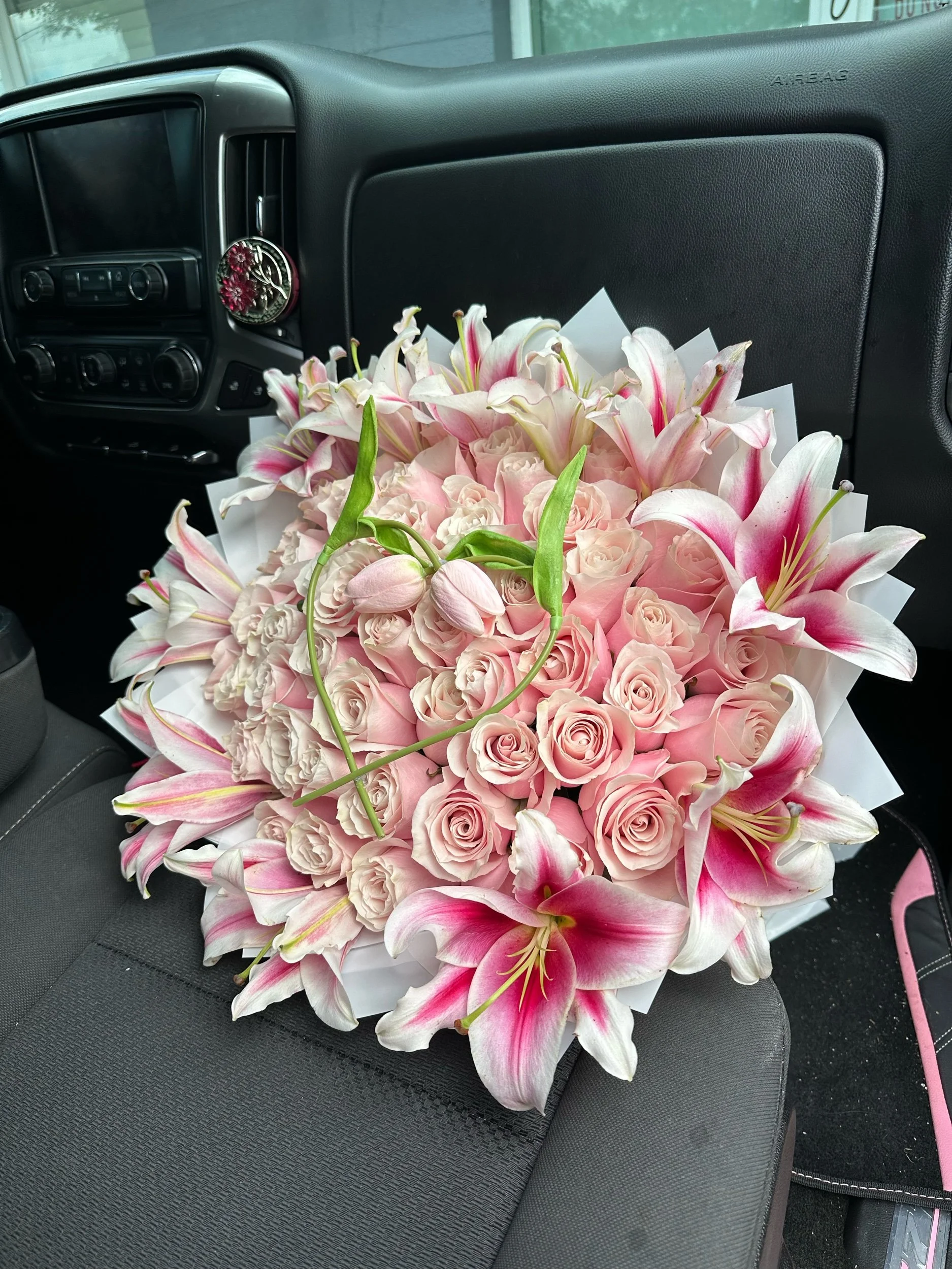 Pink rose bouquet with lilies and tulips, arranged in white waterproof floral wrapping.