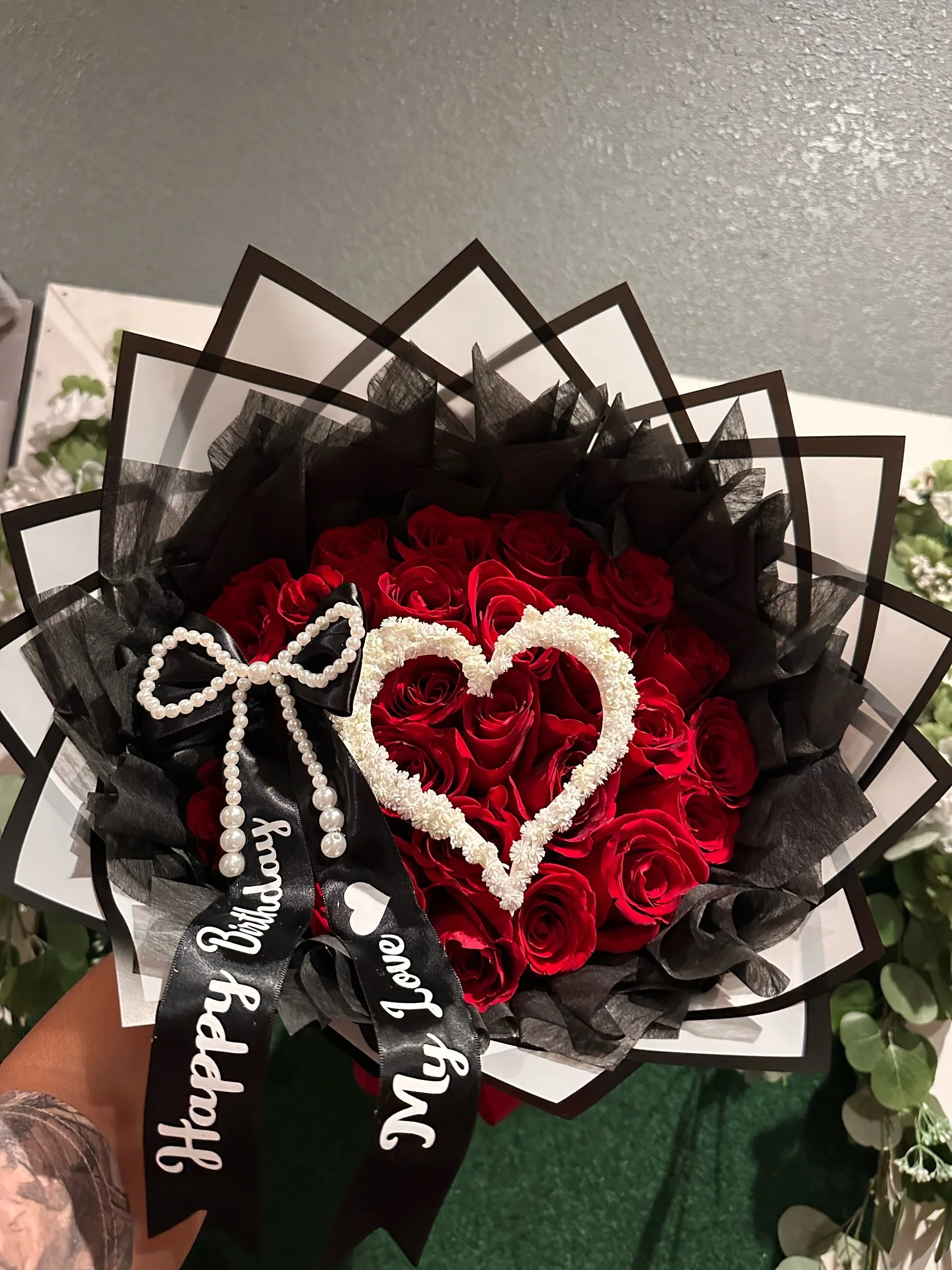 Red rose bouquet with a baby’s breath heart, pearl-accented message bow, and white floral wrapping with a black border.