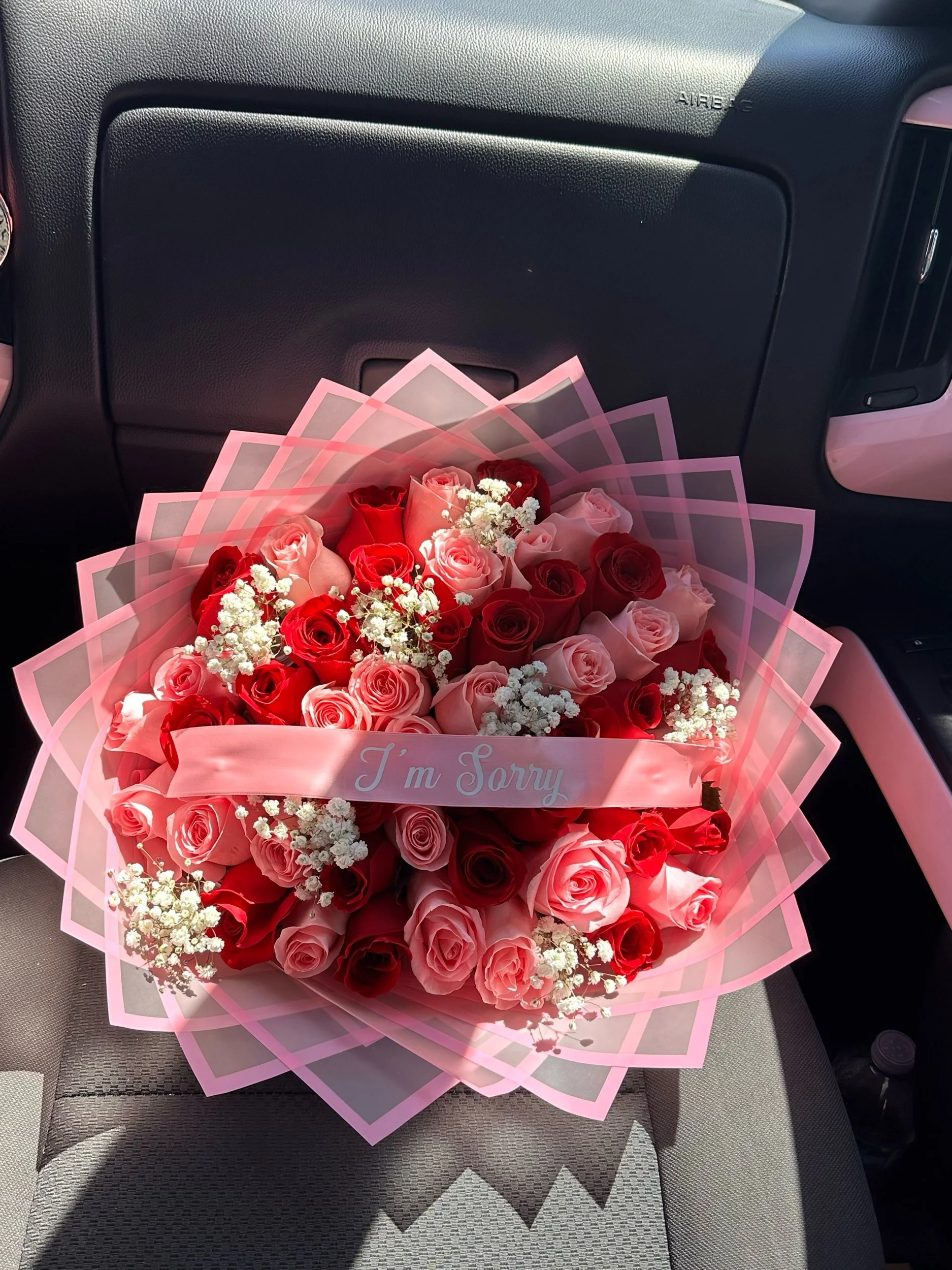 Pink and red rose bouquet with clusters of baby’s breath and a message banner, wrapped in transparent pink floral wrapping.