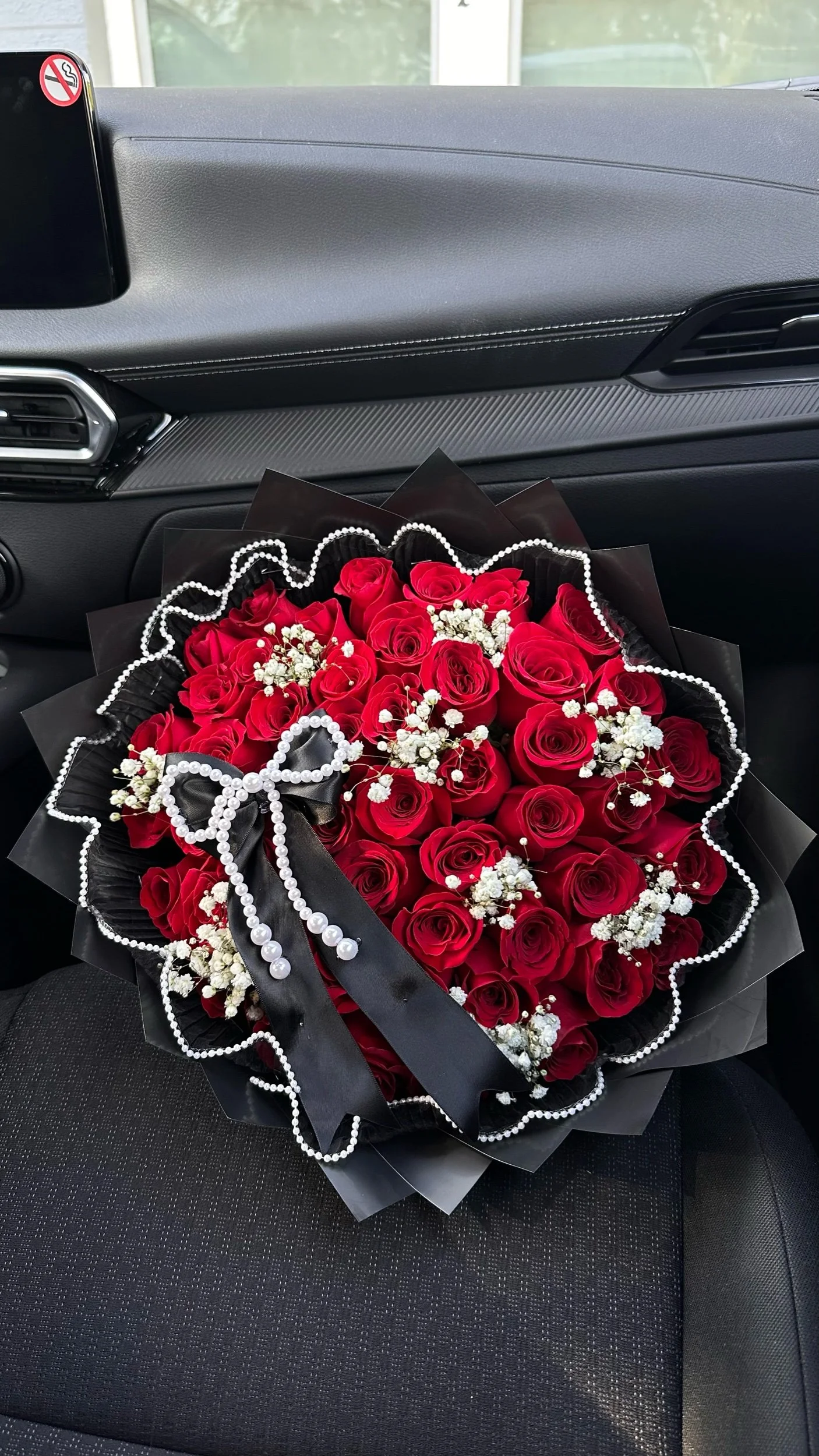 Red rose bouquet with baby’s breath, pearl mesh detailing, and a black bow, wrapped in black floral paper.