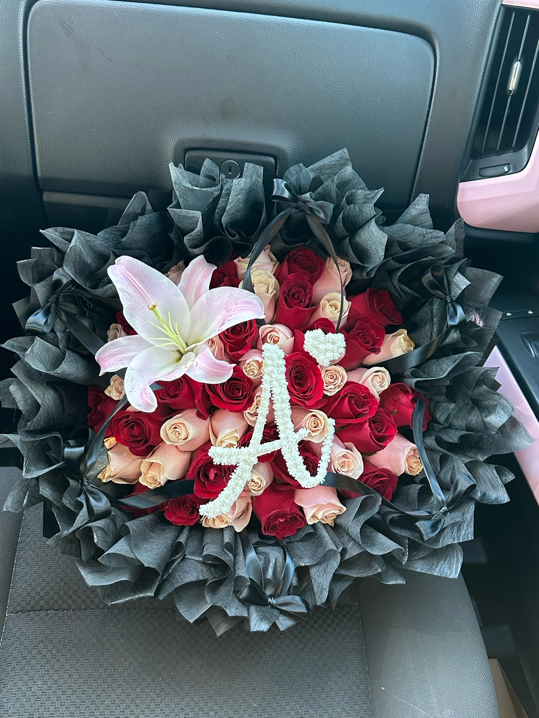 Red and pink rose bouquet with a lily and baby’s breath letter, arranged with black tissue and black waterproof floral wrapping.
