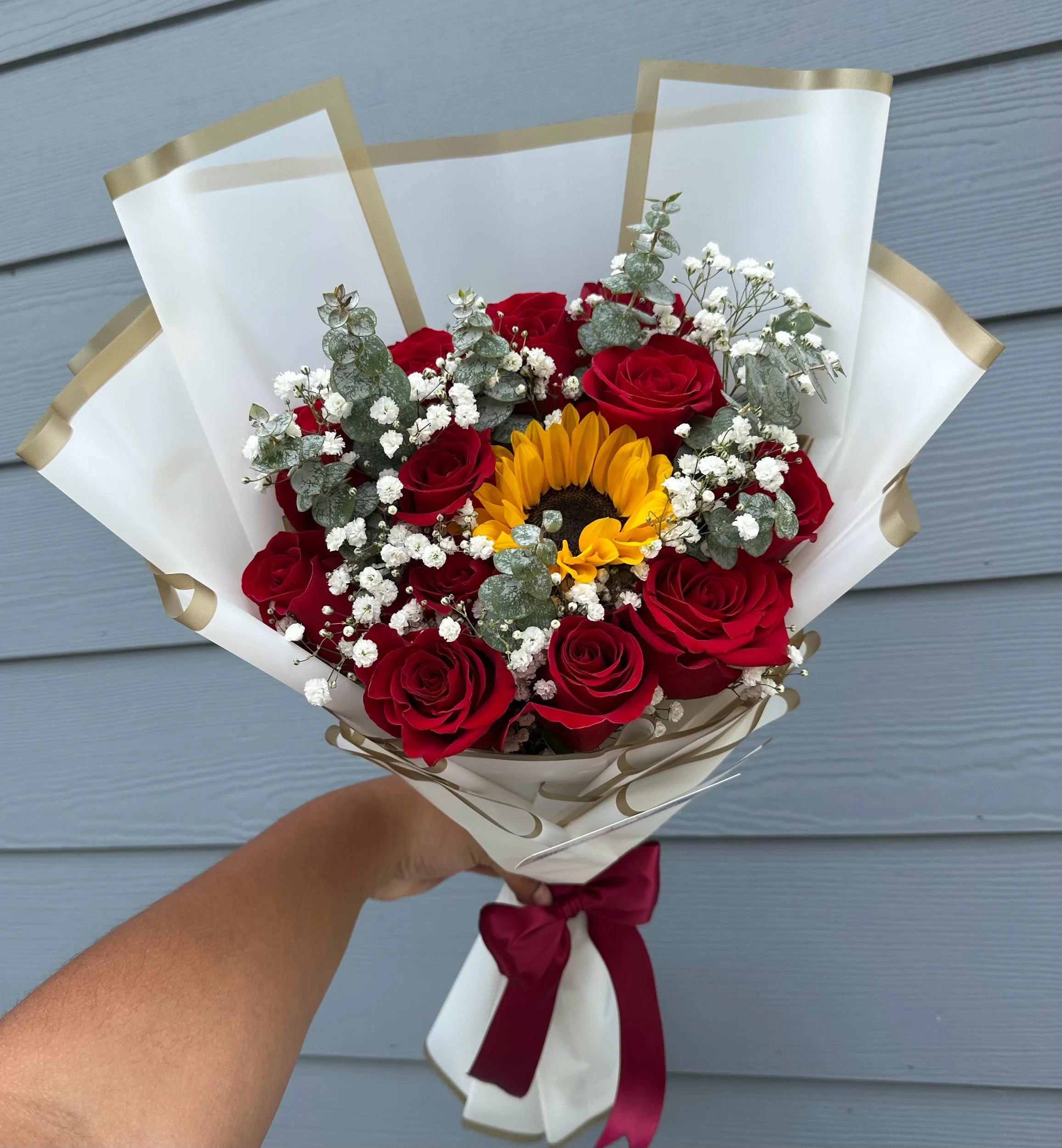 Sunflower and rose bouquet accented with baby’s breath and eucalyptus, wrapped in white floral paper with a gold border.