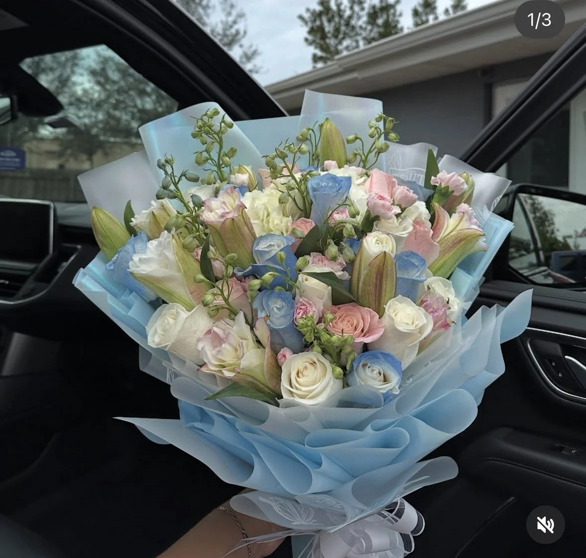 White, pink, and blue rose bouquet with delphinium, pink rose lilies, and mini pink carnations, wrapped in blue and clear butterfly floral wrapping.