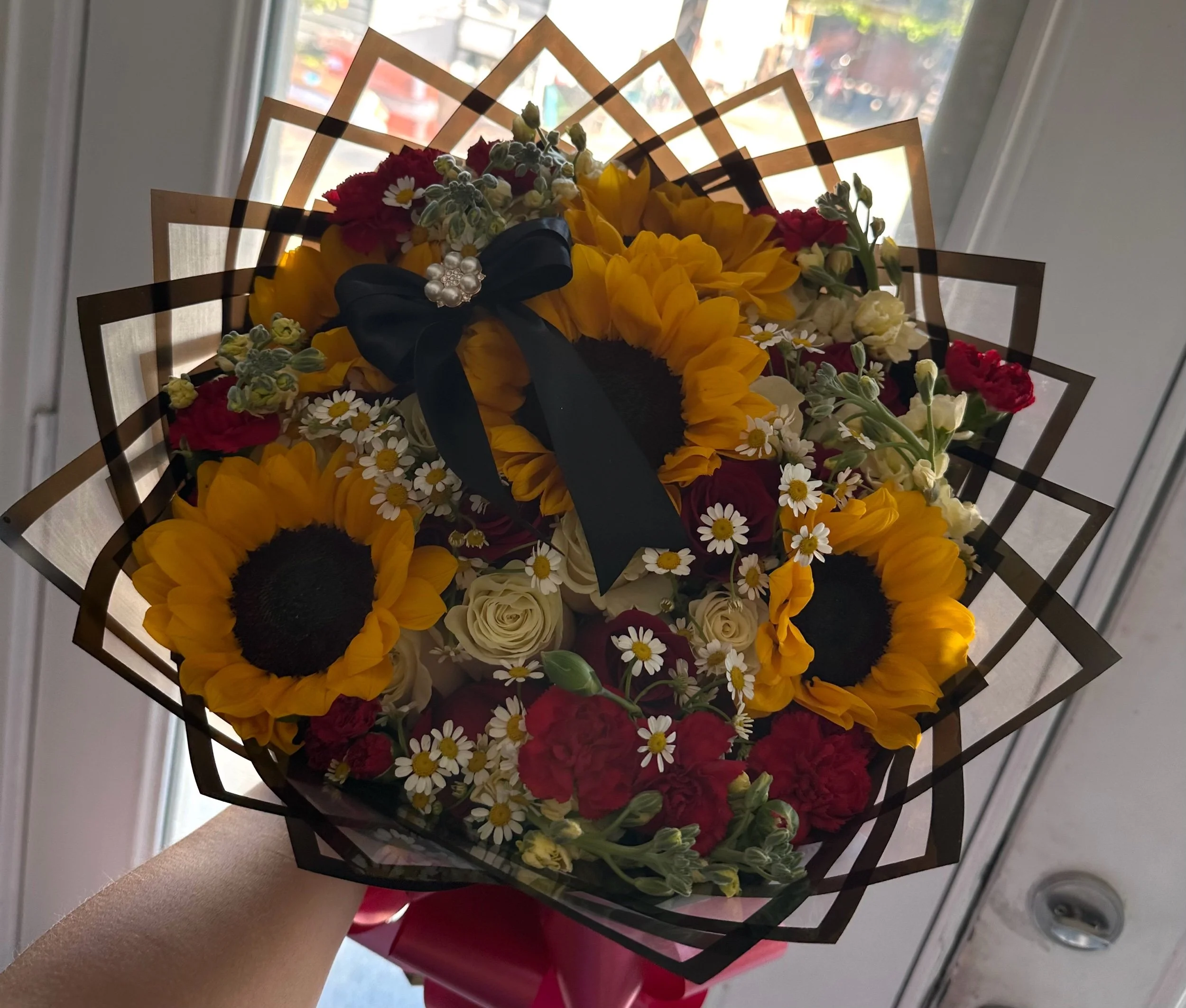 Red and white rose bouquet with sunflowers, chamomile, mini carnations, and stock, arranged in transparent black floral wrapping.