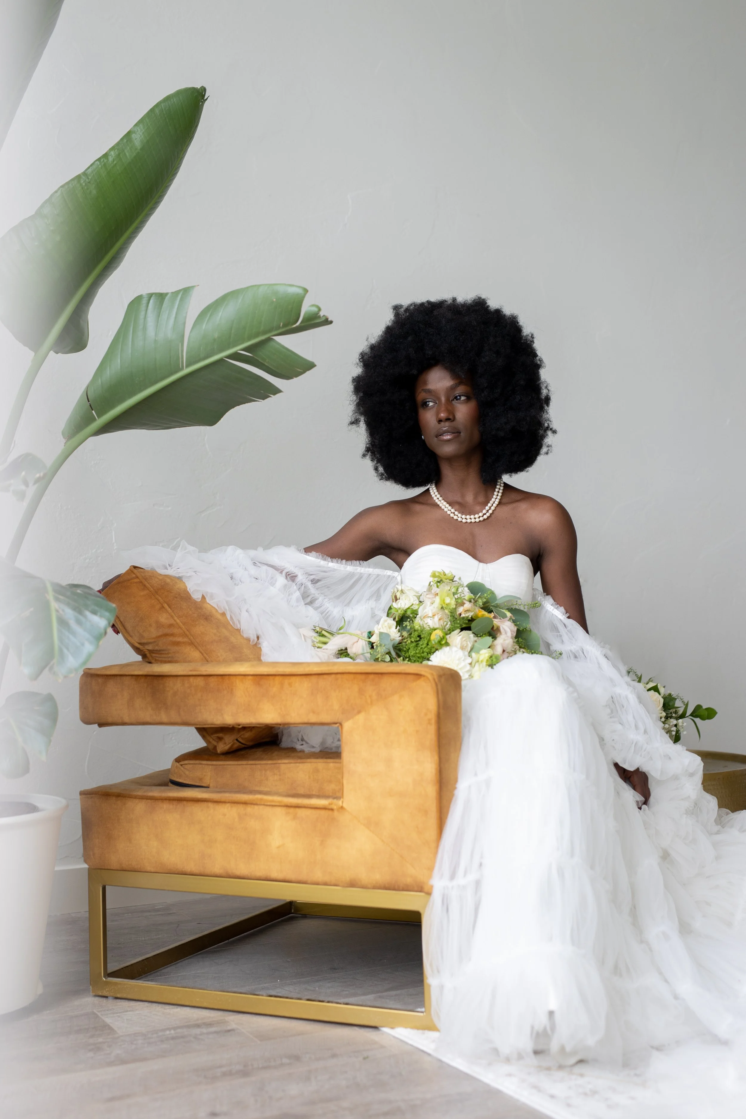 Relaxed bride lounges on a stylish couch surrounded by lush indoor plants and natural sunlight at The Ivory Hall, creating a serene bridal portrait.