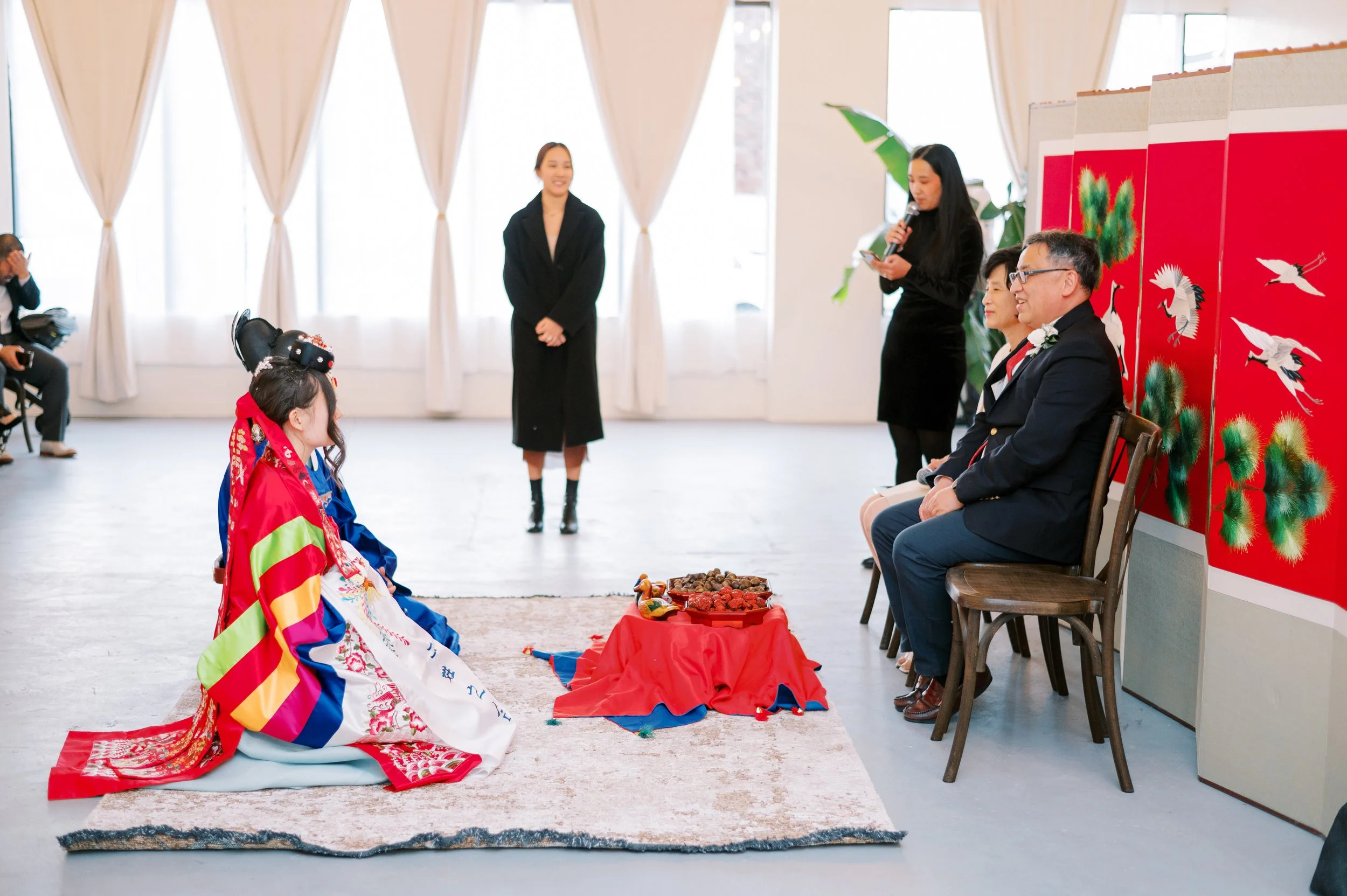 A traditional Korean wedding ceremony setup at The Ivory Hall, complete with ceremonial attire and floor cushions, beautifully framed by soft white curtains and natural light.