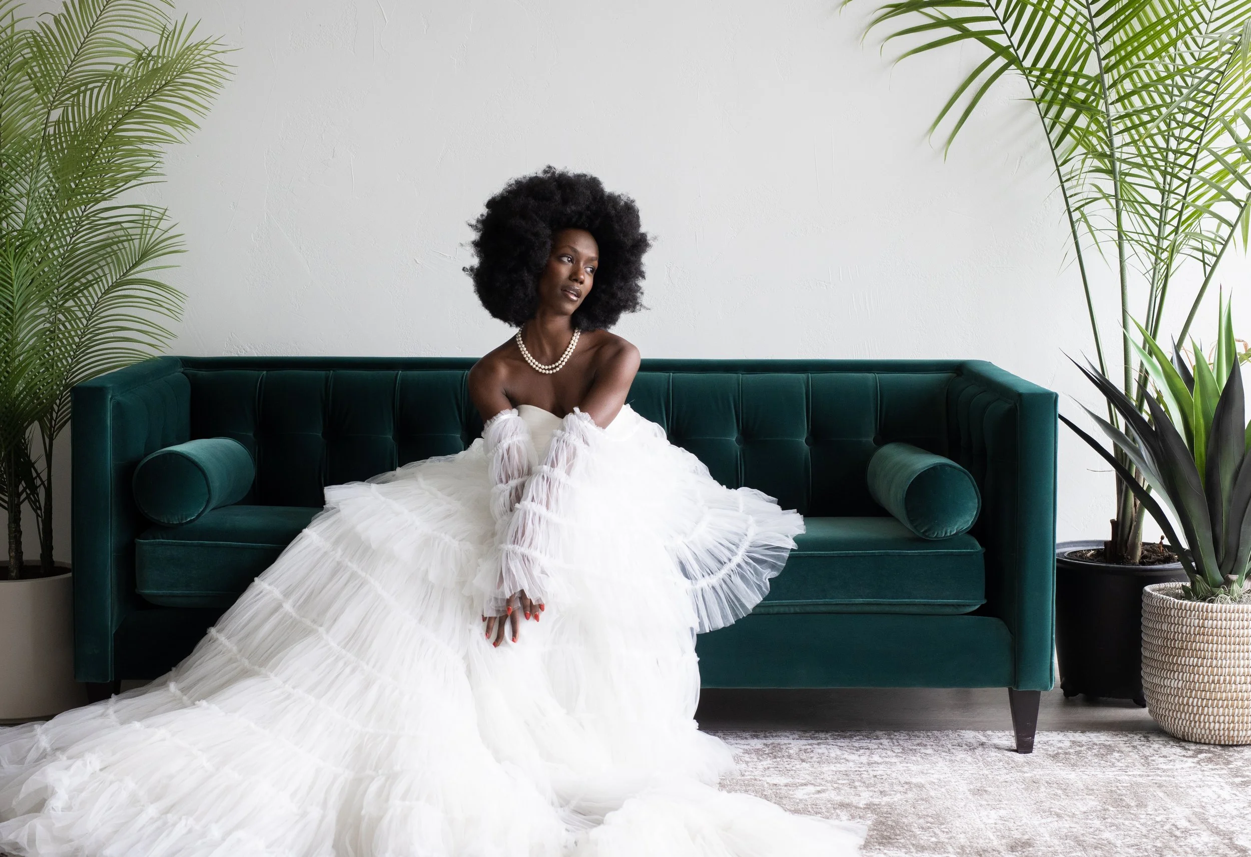 Bride in a glamorous feathered wedding gown sitting on a deep emerald green velvet couch in The Ivory Hall bridal suite, showcasing elegant textures and natural light.